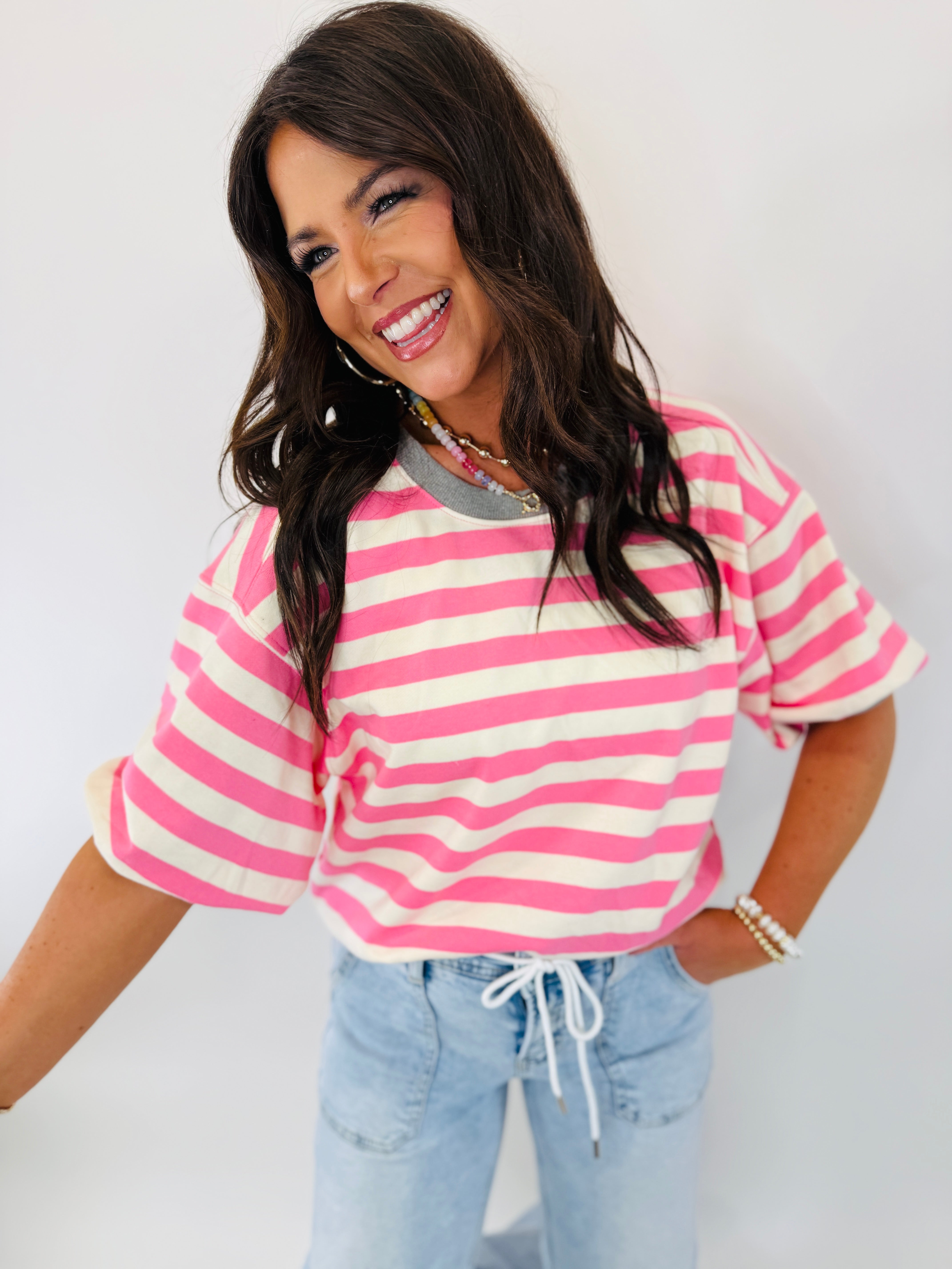 Woman wearing pink and white striped short-sleeve top with light blue drawstring pants, smiling at camera.