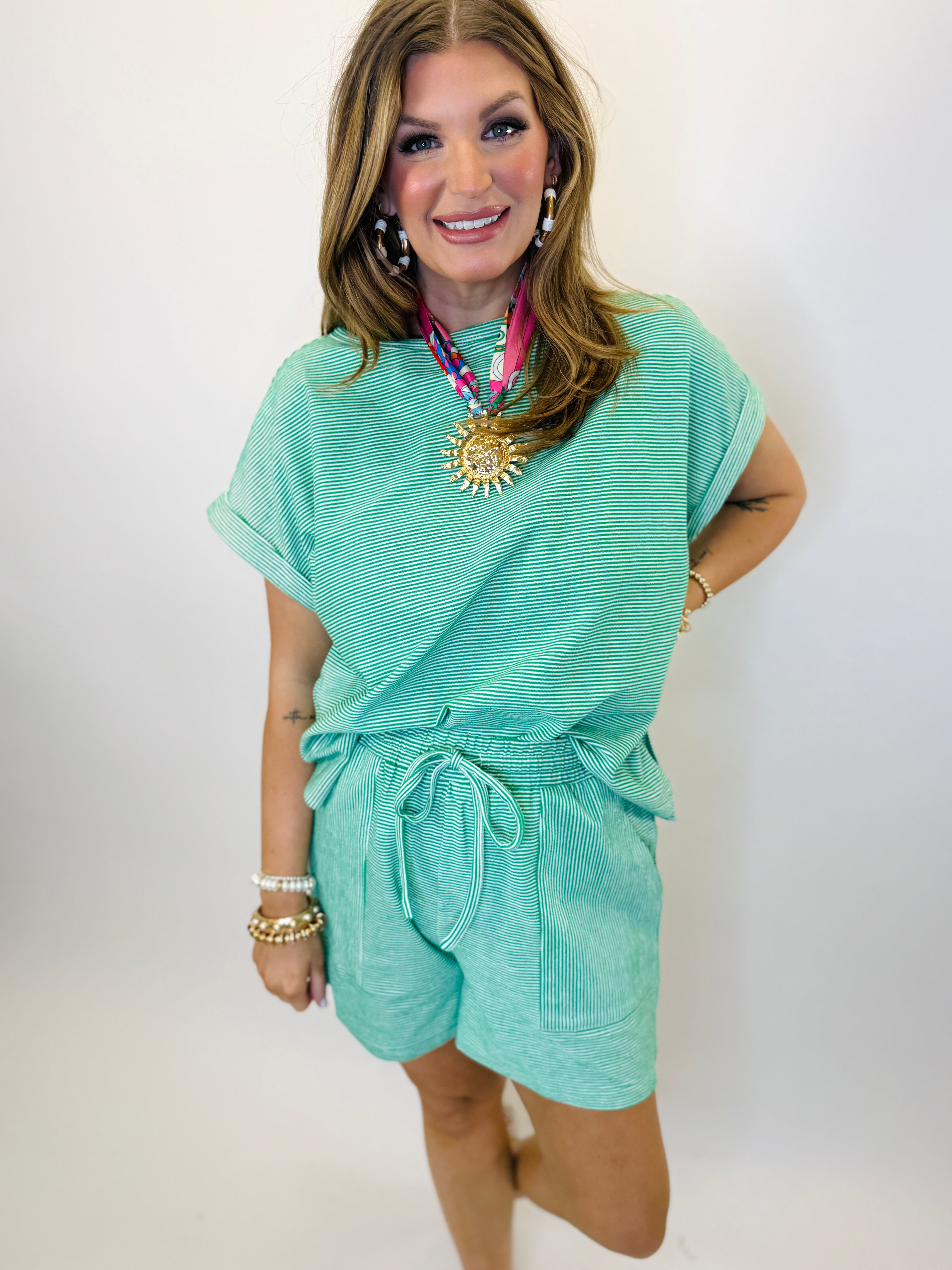 Woman wearing turquoise striped short-sleeve top and matching shorts set with tie waist and pockets.