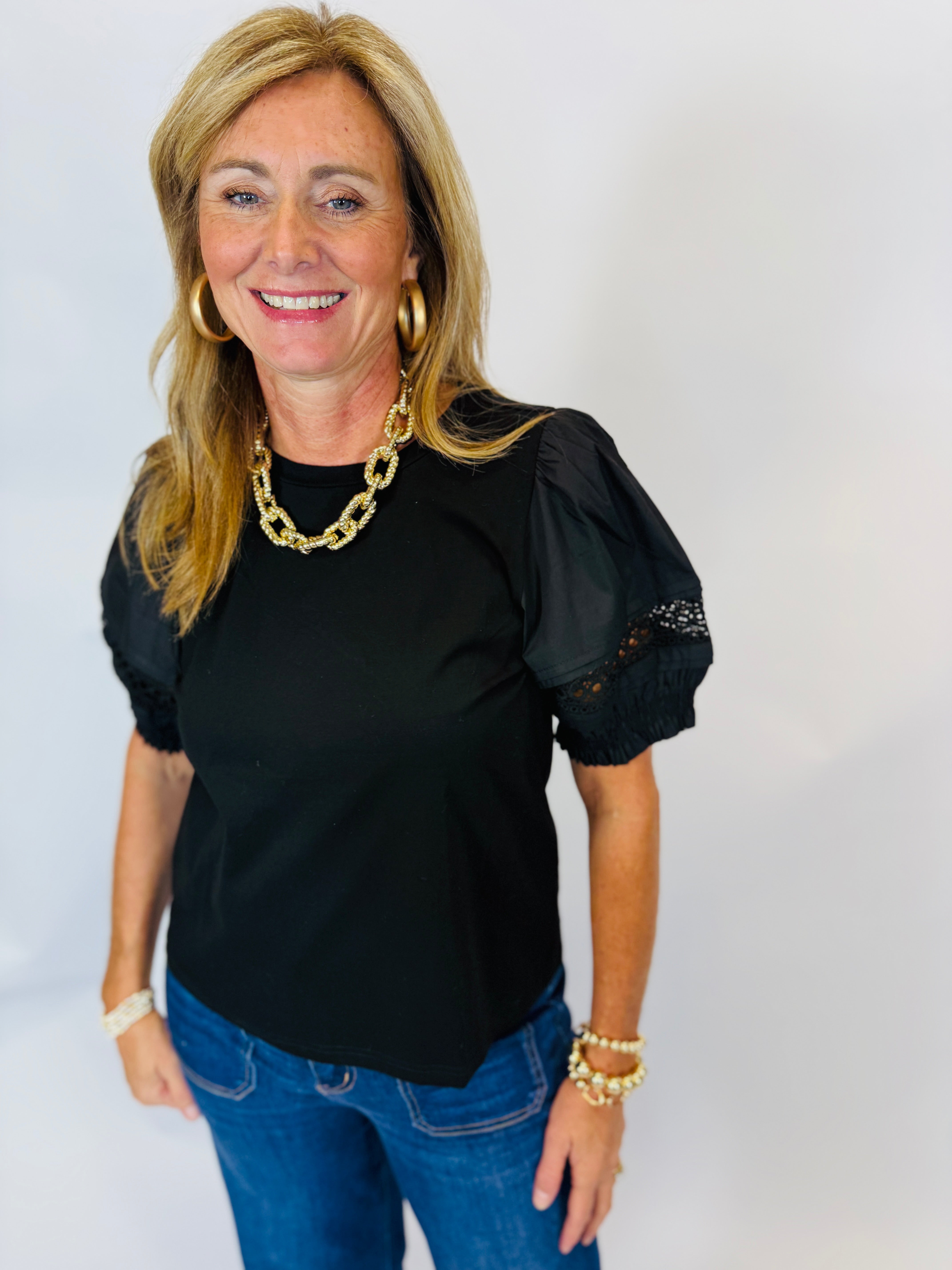 Woman wearing black Jenna Top with puff sleeves and lace trim, paired with blue jeans.