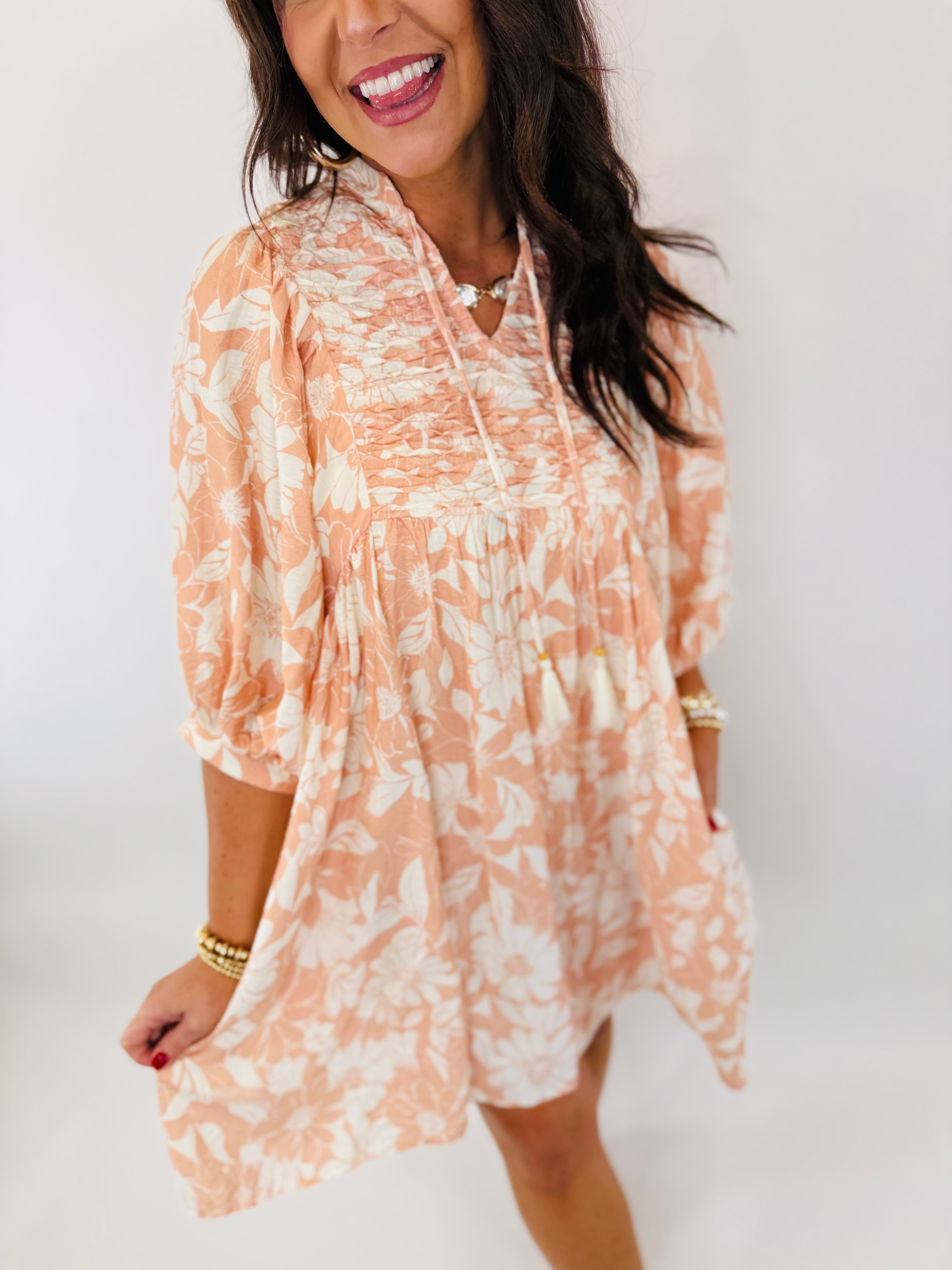 Woman wearing peach floral print mini dress with ruffled neckline and three-quarter sleeves