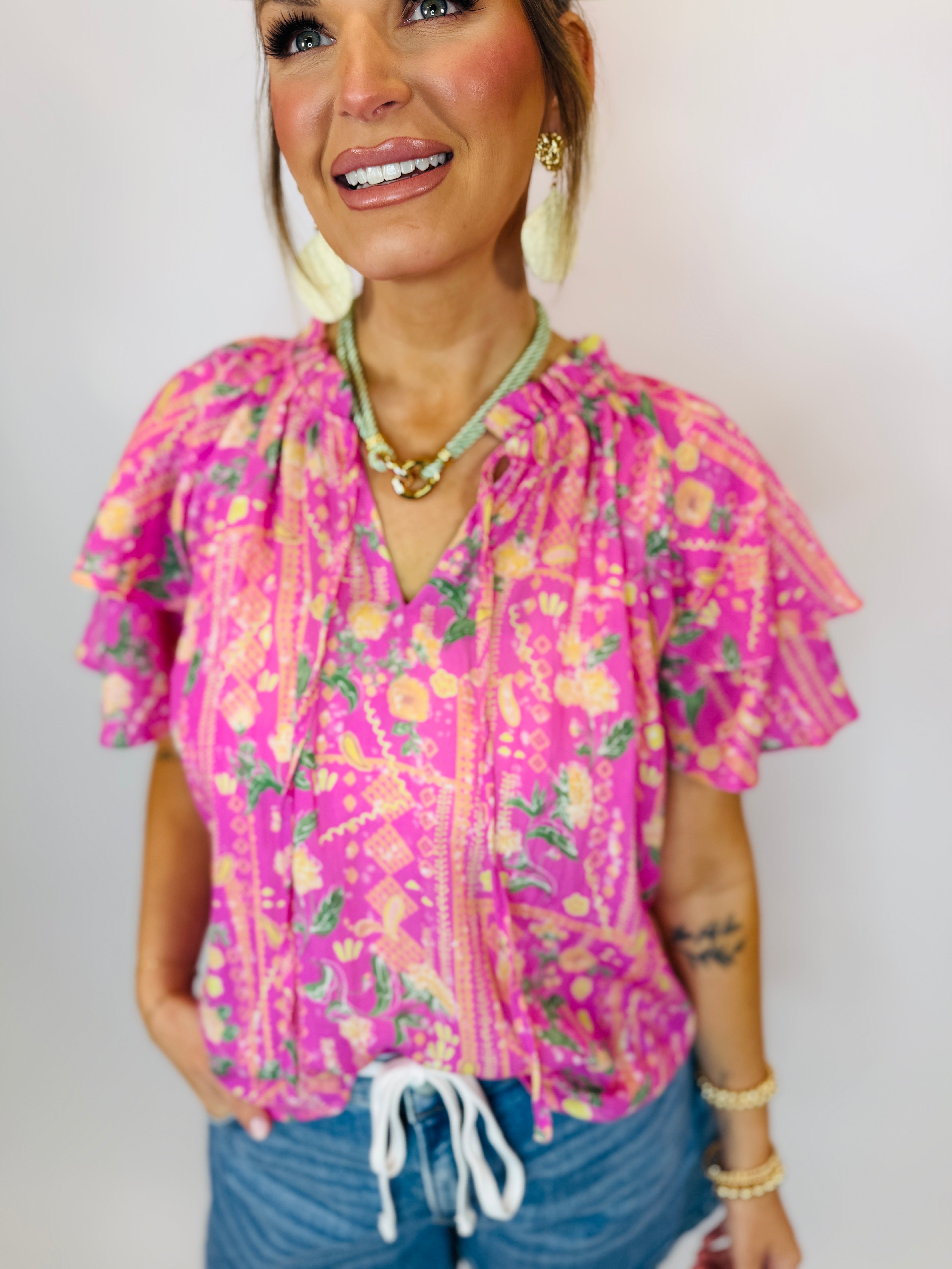 Bright pink floral print Denisse top with ruffled sleeves and tie-front detail on smiling woman