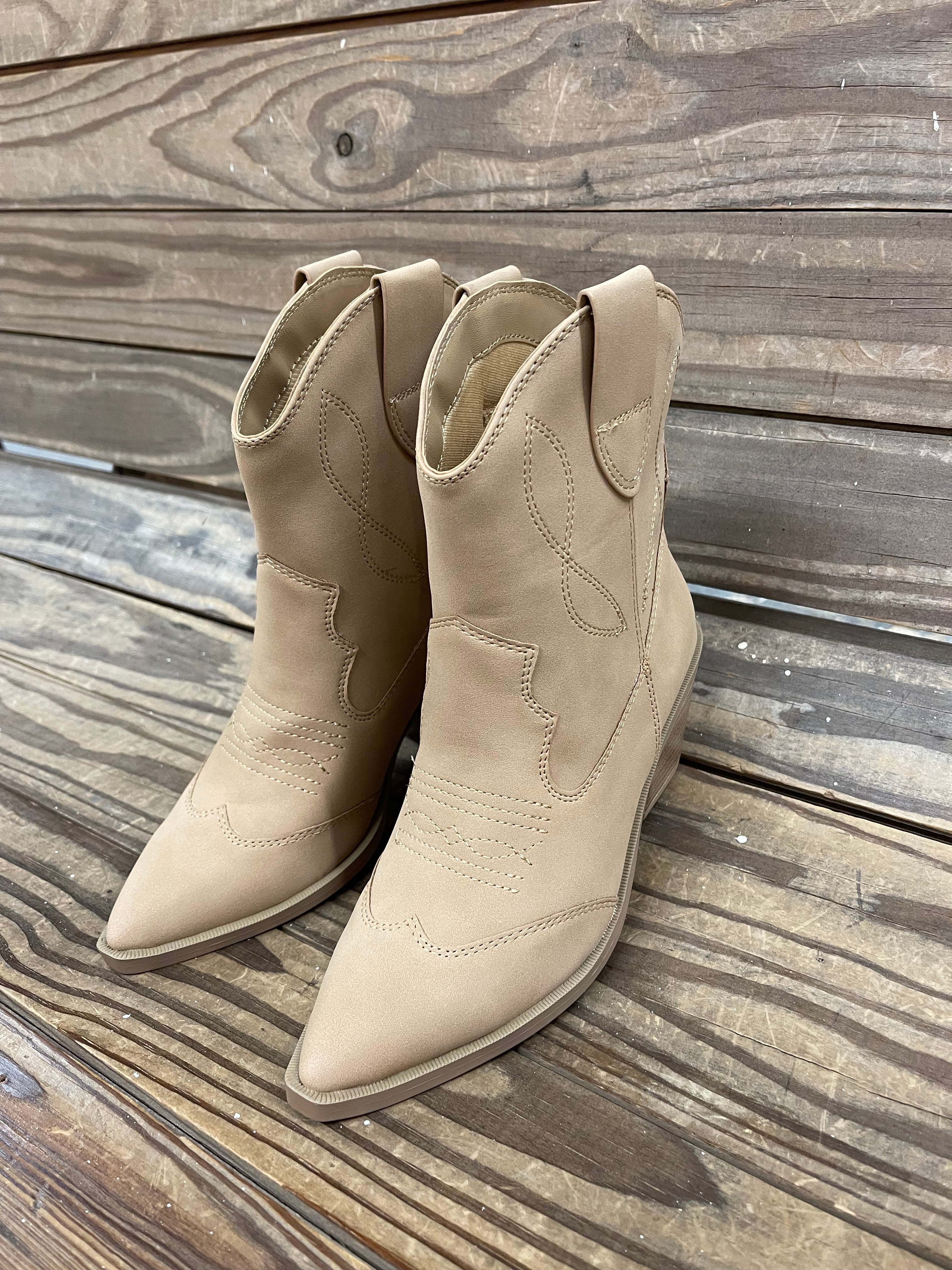 Tan suede pointed-toe cowboy boots with decorative stitching on weathered wood surface