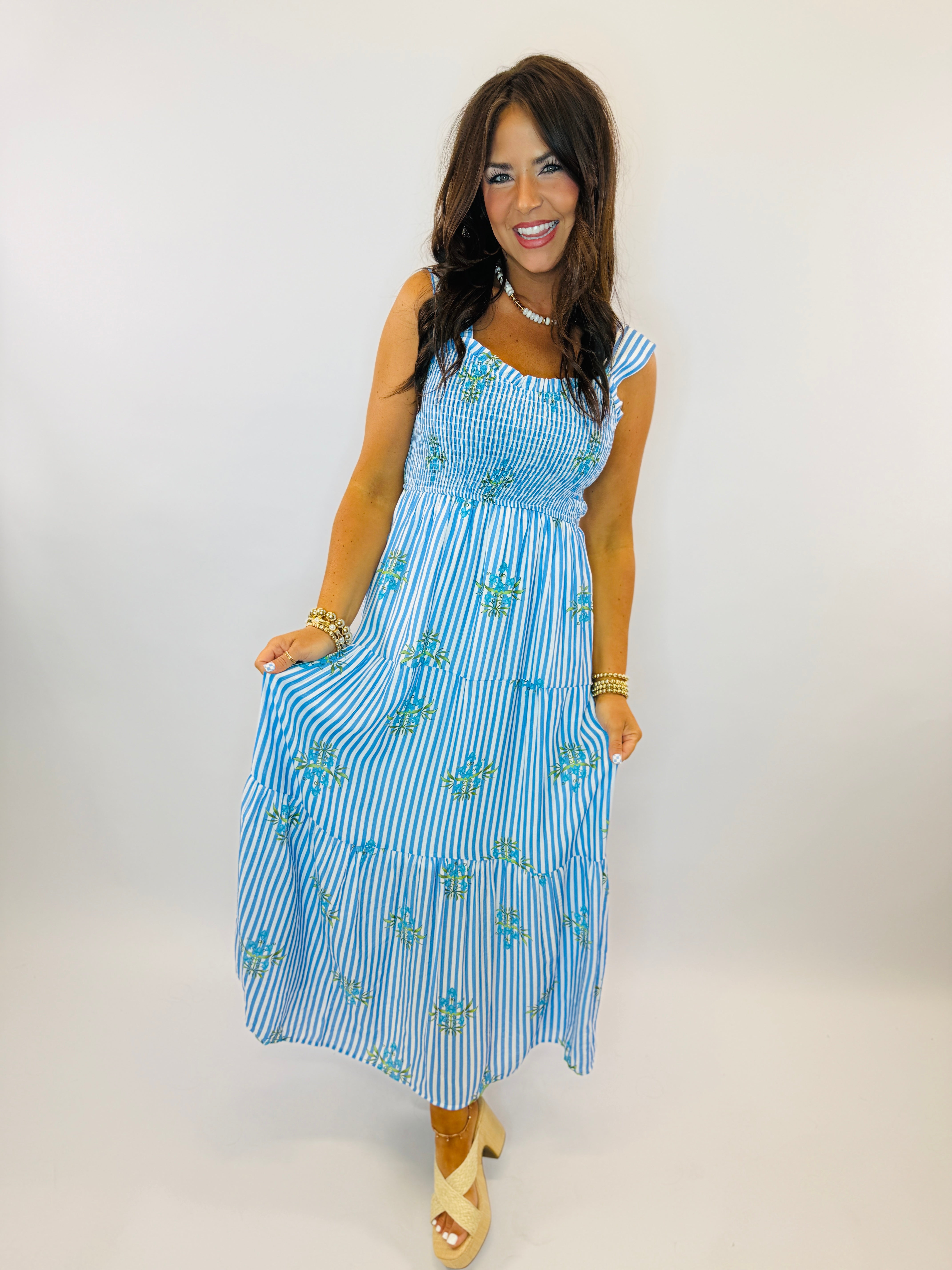 Woman wearing blue and white striped midi dress with floral embroidery, smocked bodice, and tiered skirt