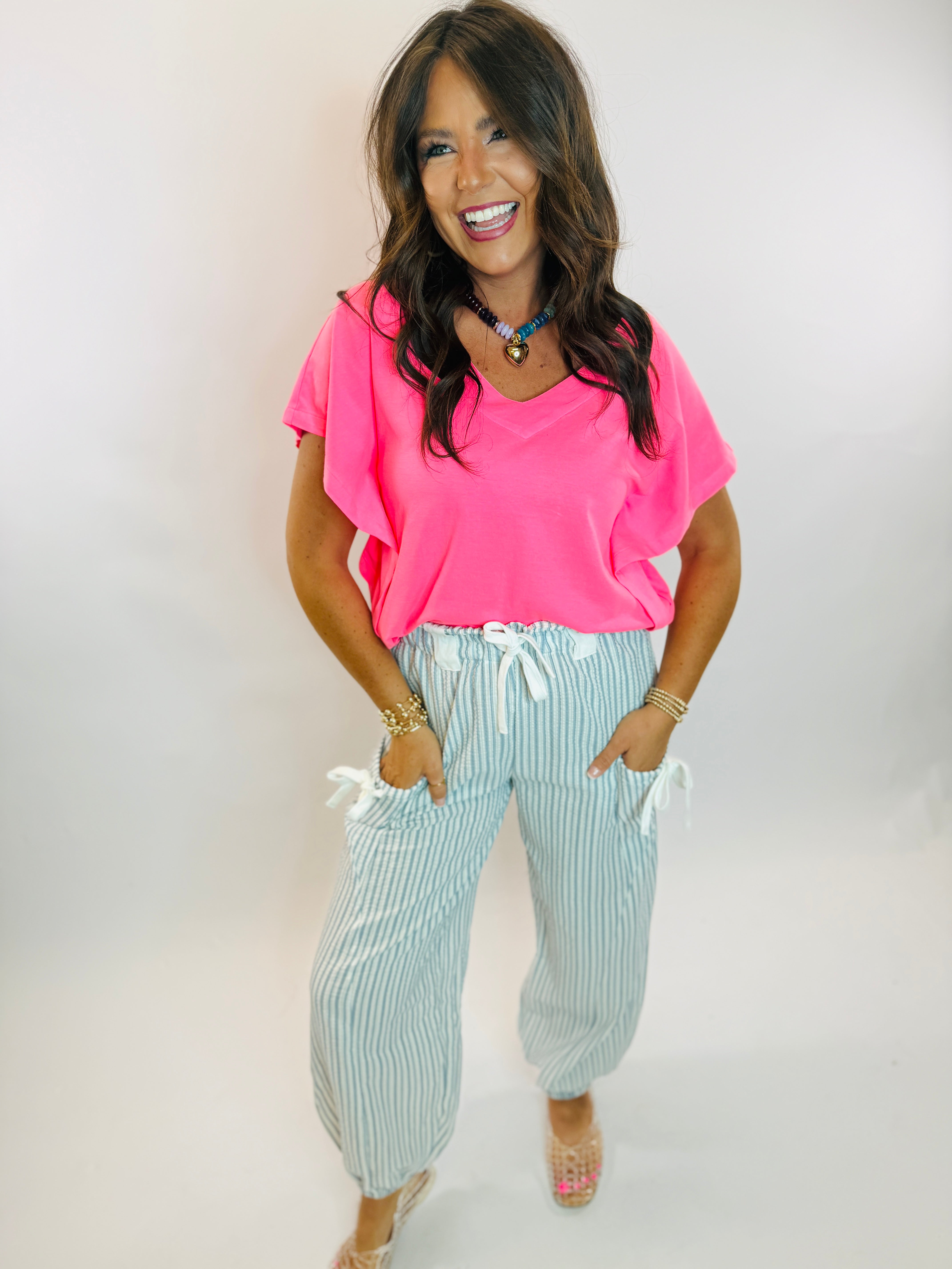 Woman wearing a neon pink v-neck short sleeve top paired with striped drawstring jogger pants.