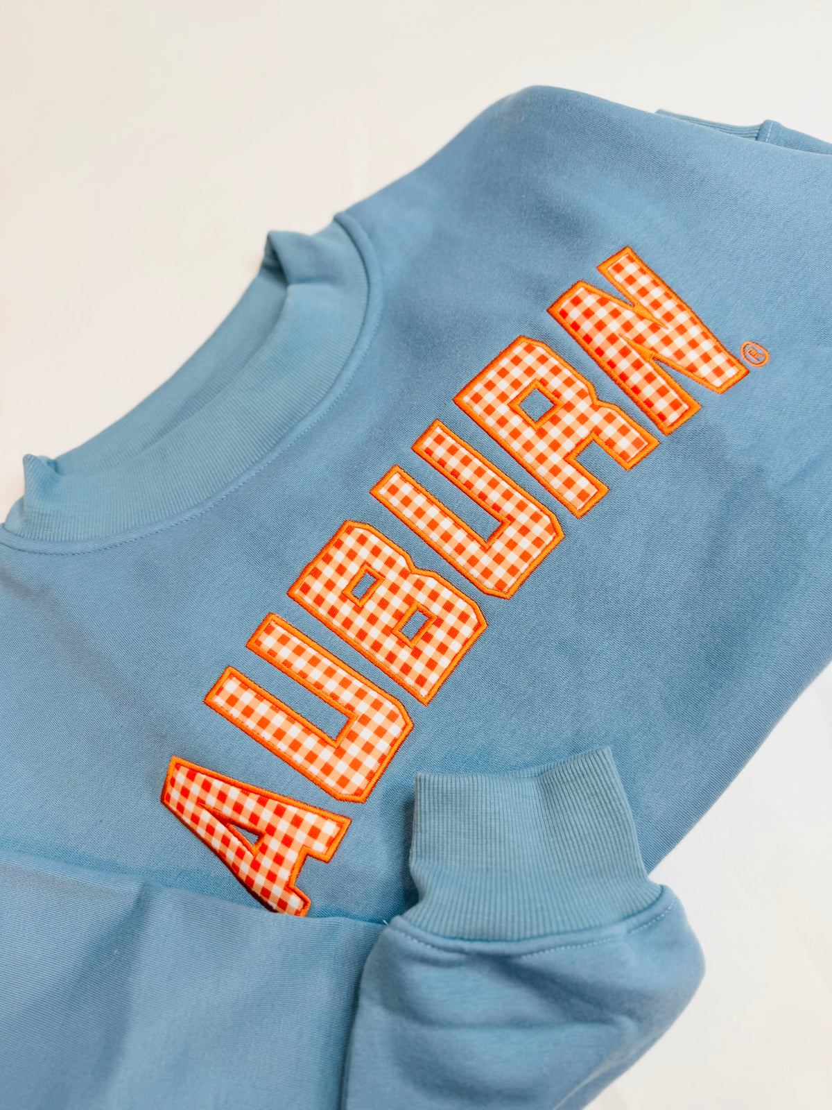 Light blue crewneck sweatshirt featuring orange gingham appliqué "AUBURN" lettering on the chest.