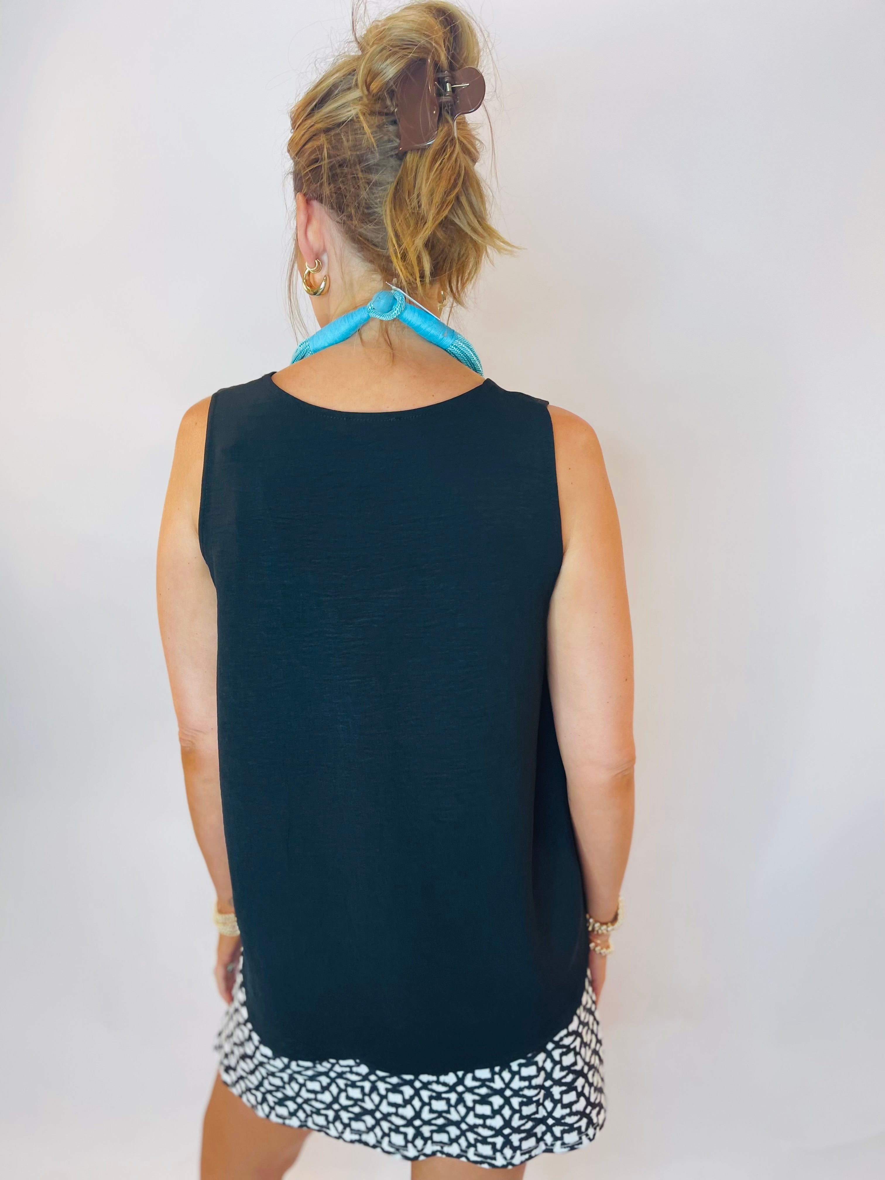 Woman wearing a sleeveless black tank top with a black and white patterned skirt, viewed from behind.