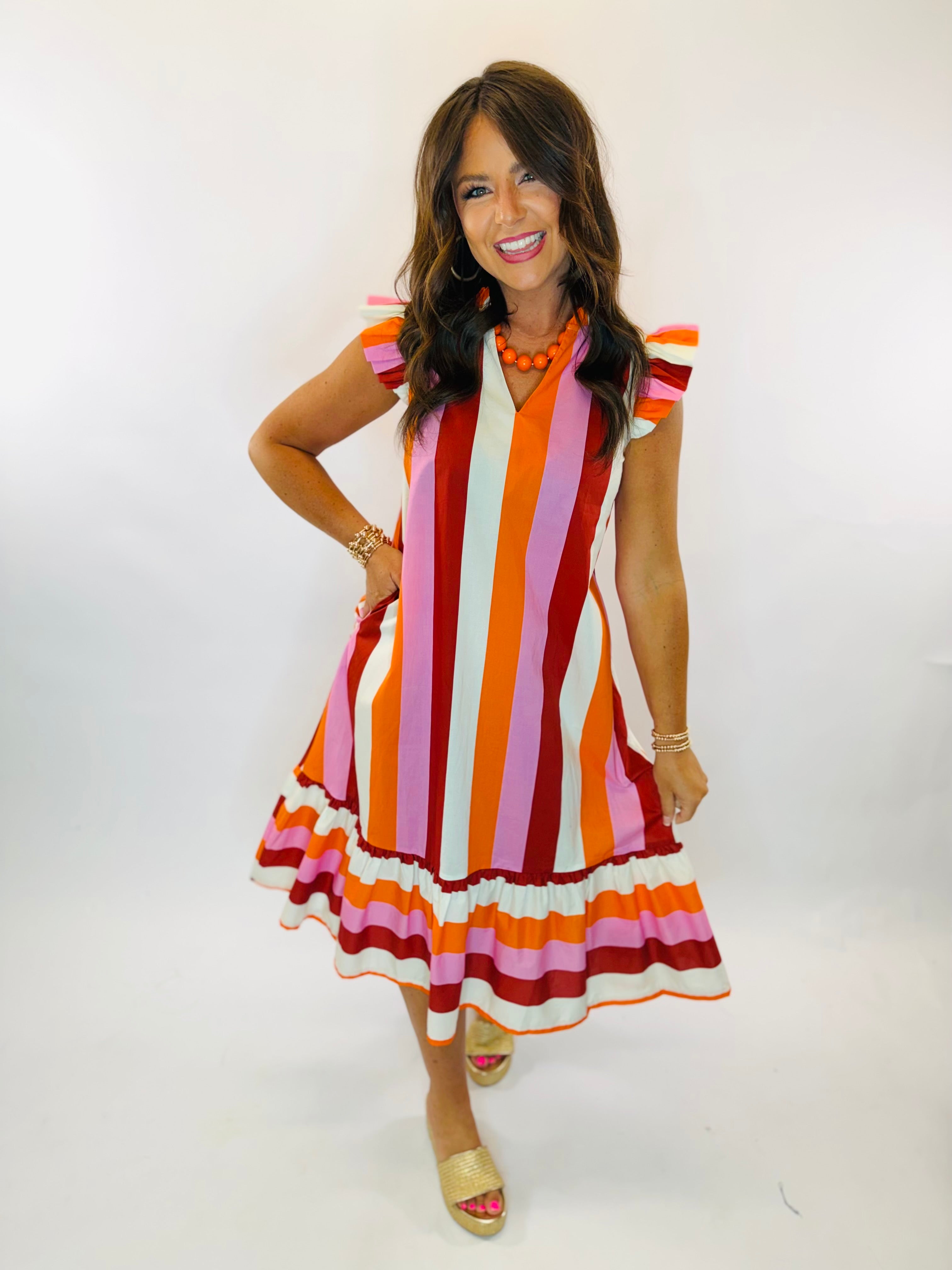 Woman wearing Lola Midi dress with bold multicolor vertical stripes, ruffle hem, and flutter sleeves.
