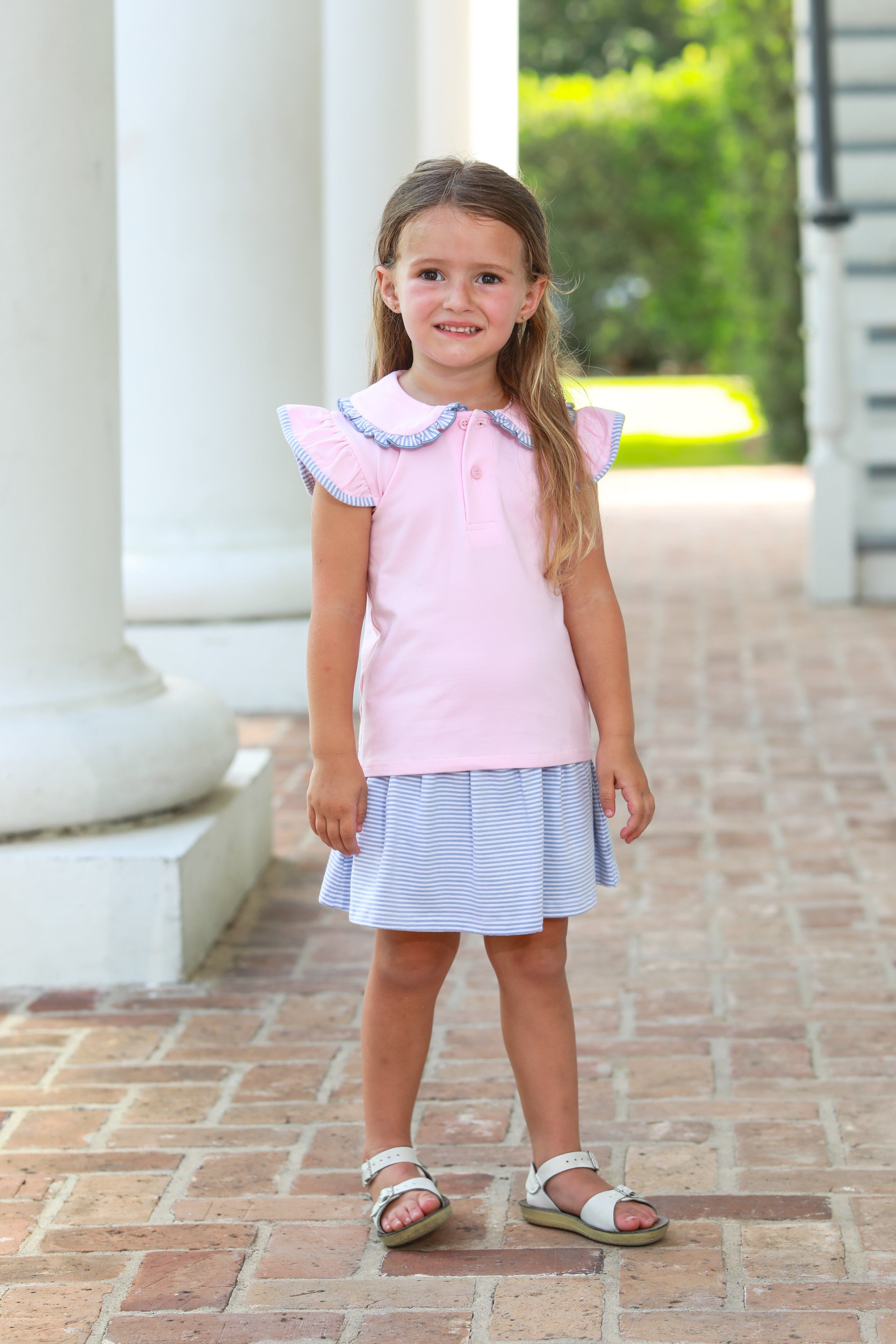 Young girl wearing pink ruffled top with blue striped collar and matching blue striped skort set