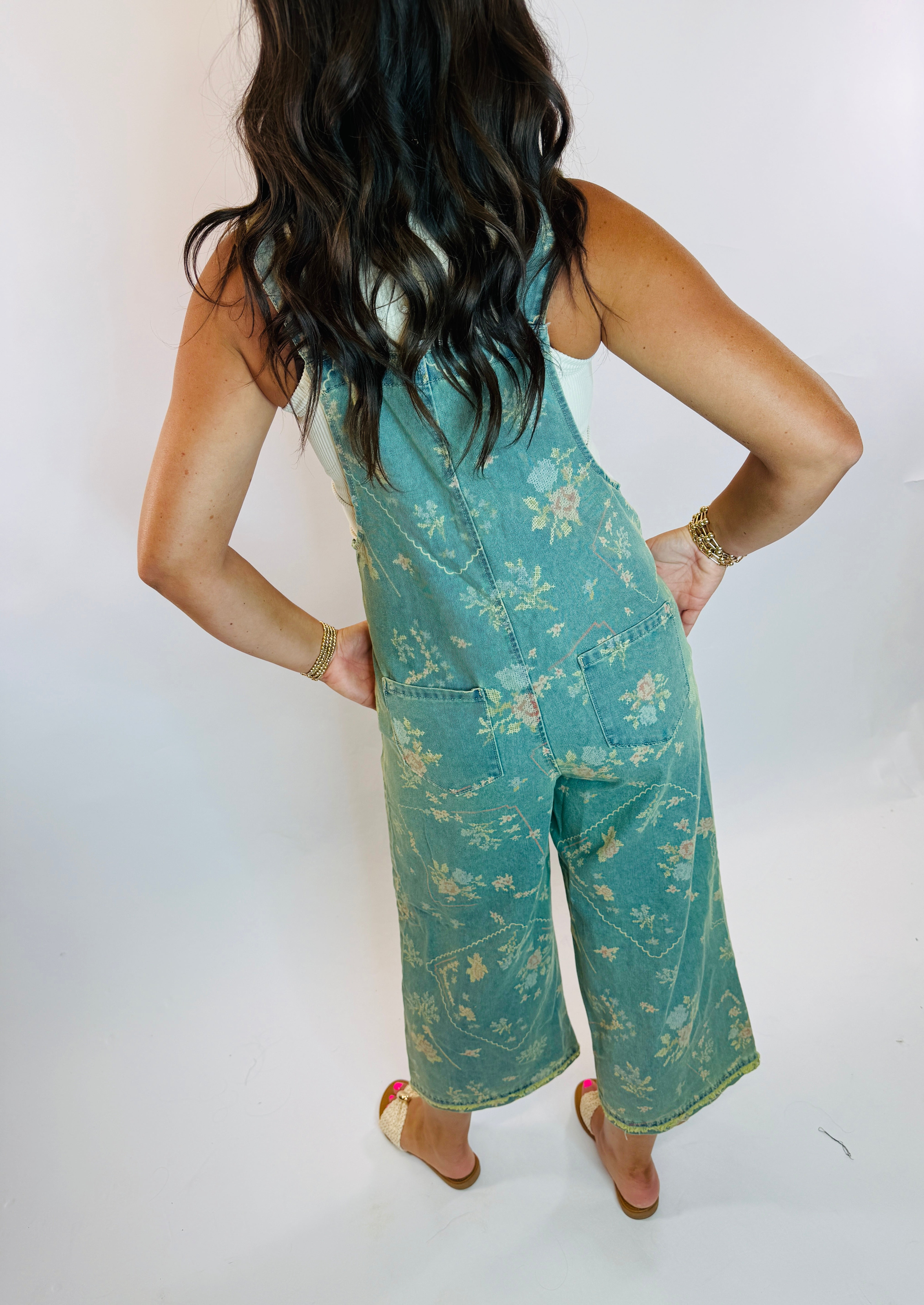 Woman wearing teal floral-print wide-leg denim overalls with back pockets, shown from behind.