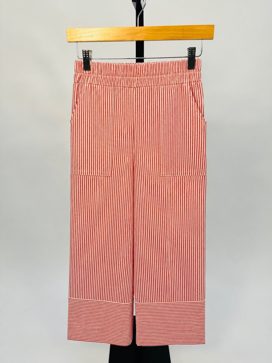 Red and white striped wide-leg pants with elastic waistband hanging on wooden hanger against gray background.
