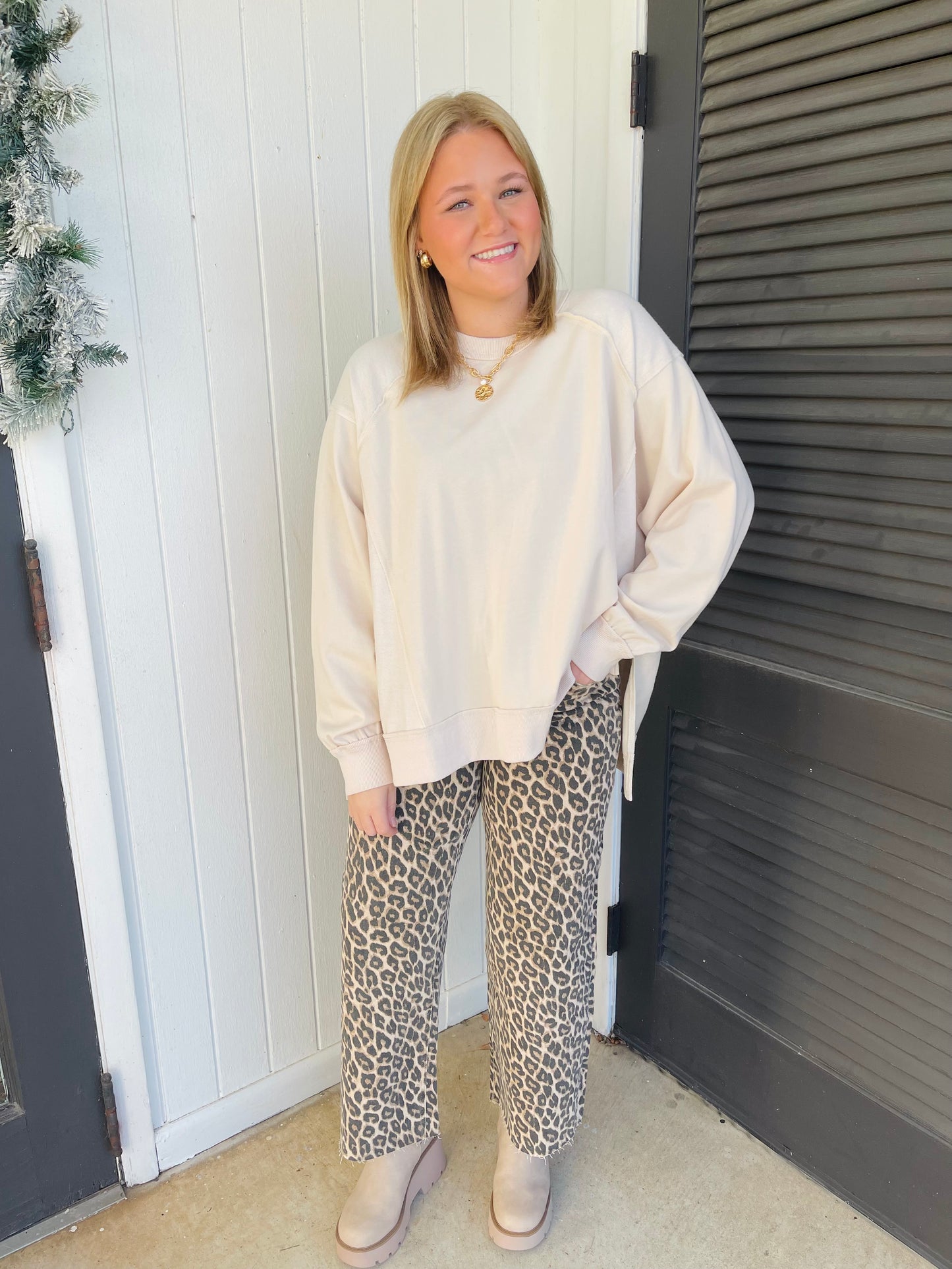 Woman wearing cream oversized sweatshirt with leopard print pants and beige shoes, standing outdoors