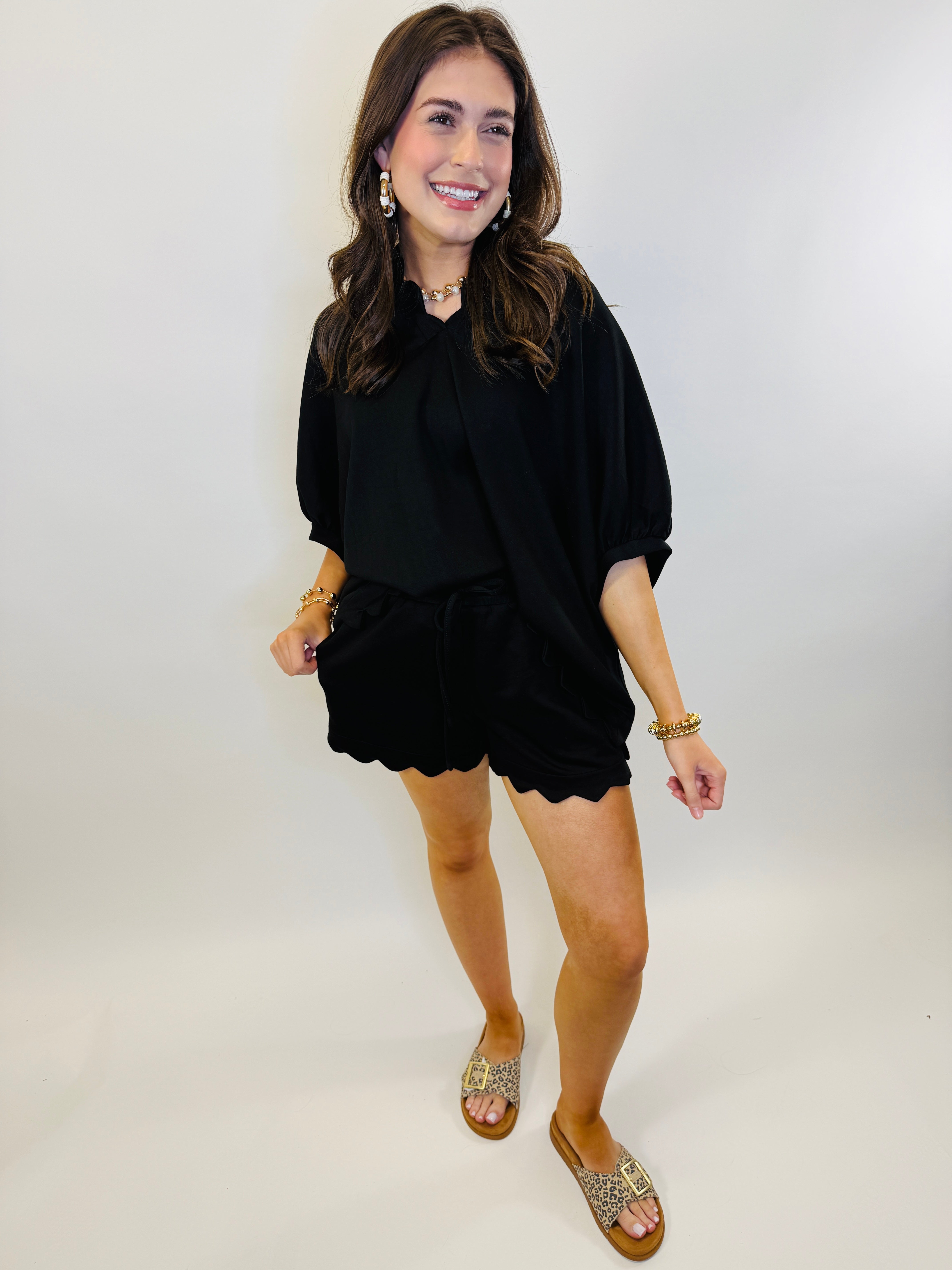 Woman wearing black oversized top and matching shorts set with gold jewelry and leopard print sandals