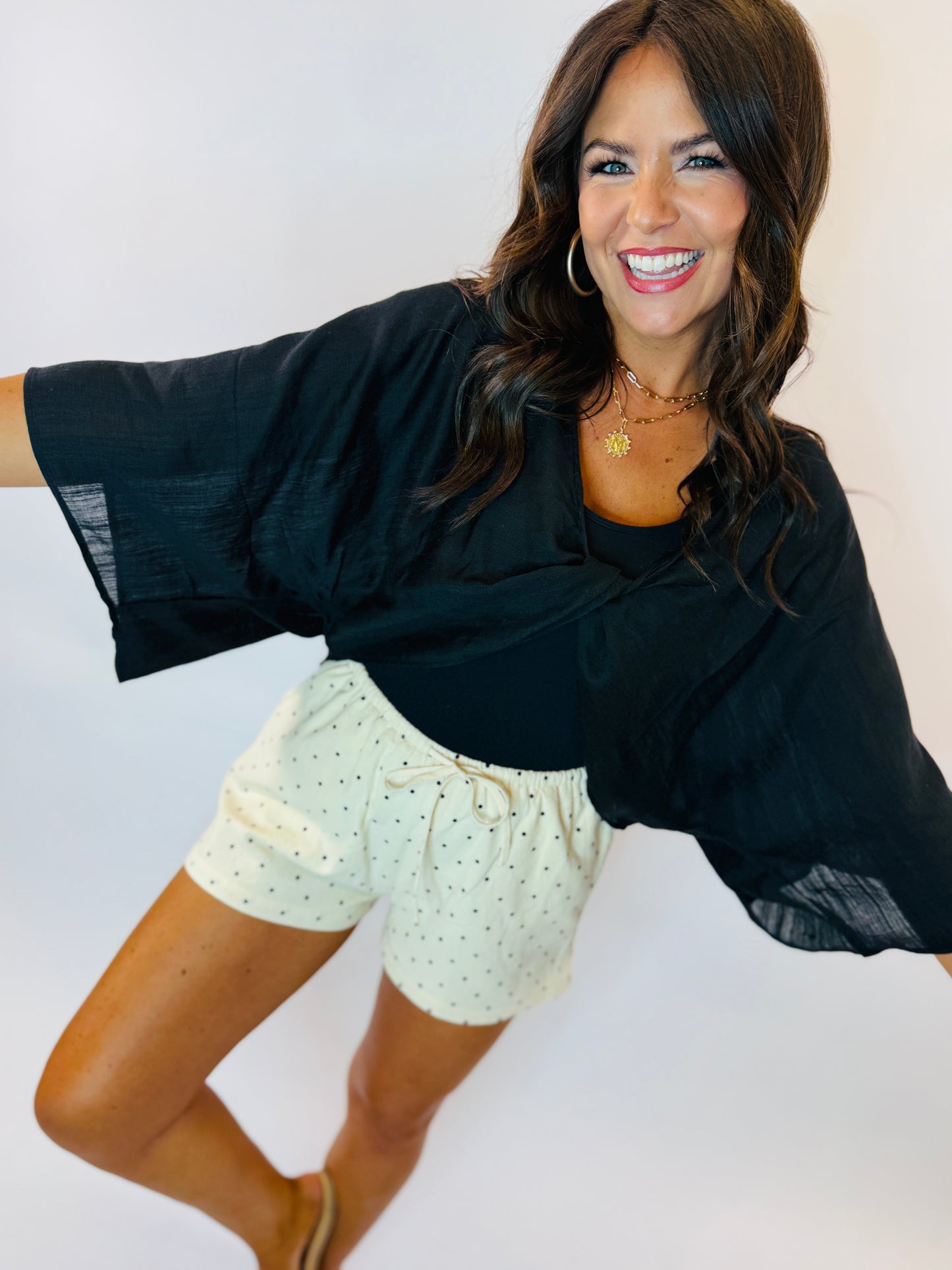 Woman wearing light green polka dot drawstring shorts with black long-sleeve top, smiling and posing
