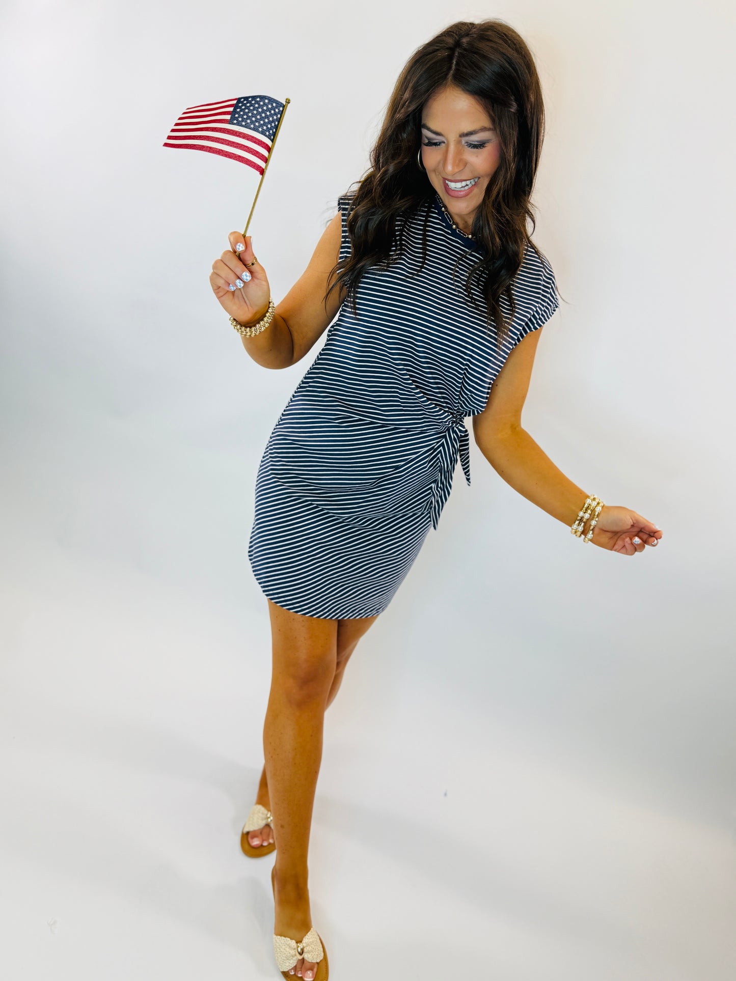 Woman wearing navy and white striped Jonah dress with tie waist detail, holding small American flag