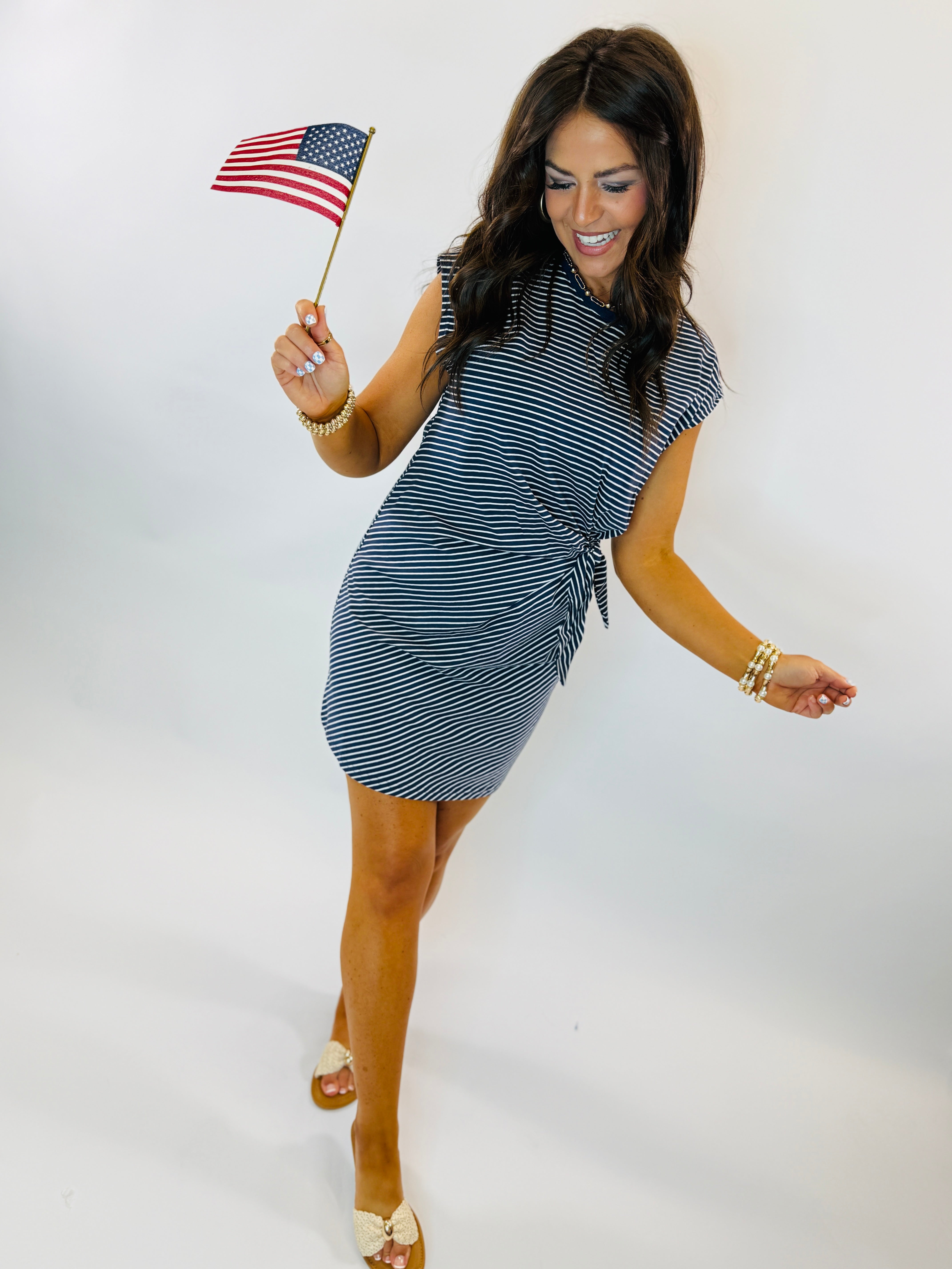 Woman wearing navy and white striped Jonah dress with tie waist detail, holding small American flag