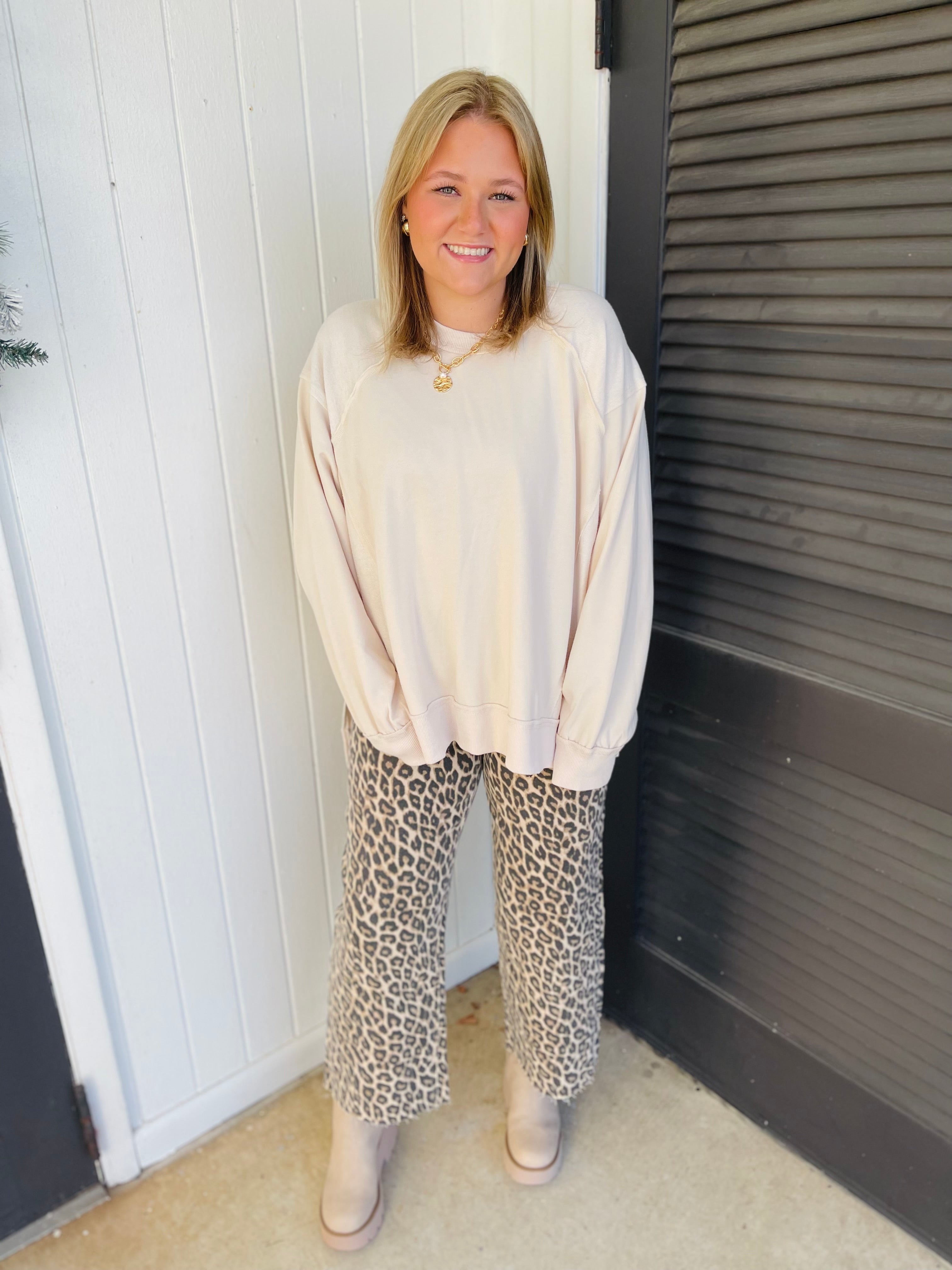 Woman wearing cream oversized Rory sweatshirt with leopard print pants and beige shoes, smiling outdoors