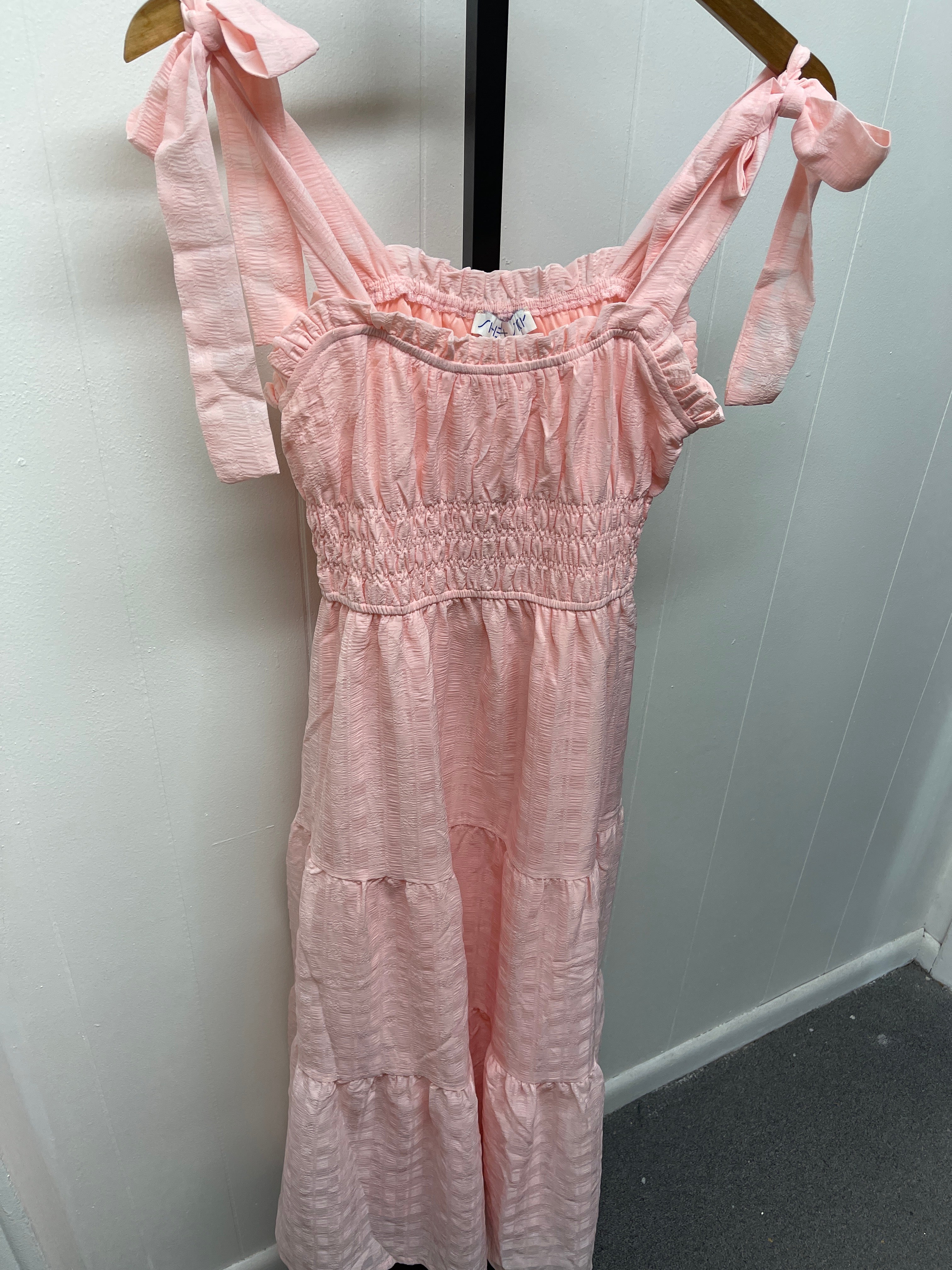 Pink tiered midi dress with tie shoulder straps and smocked bodice hanging on wooden hanger