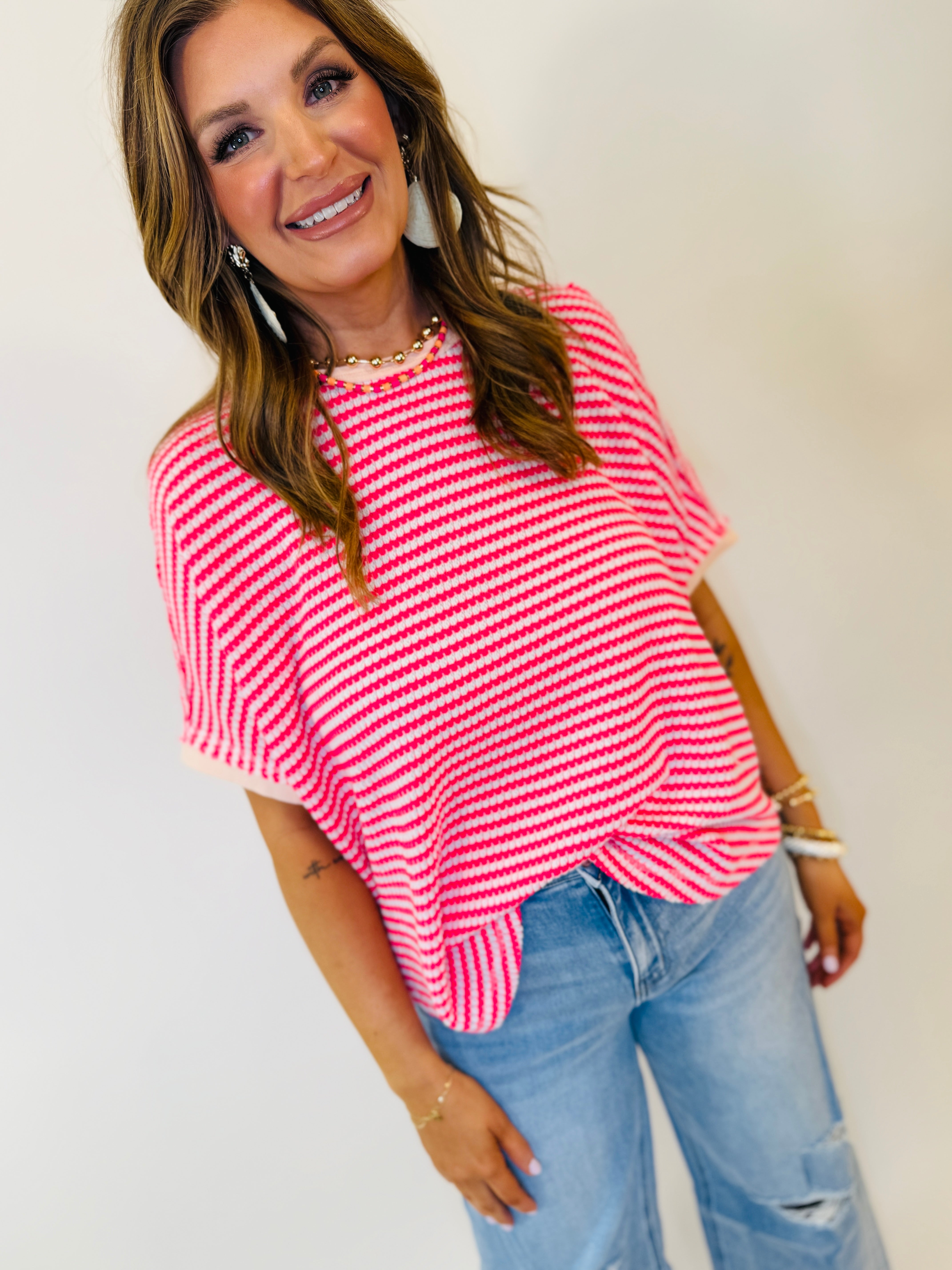 Woman wearing pink and white striped oversized top with blue distressed jeans and gold jewelry