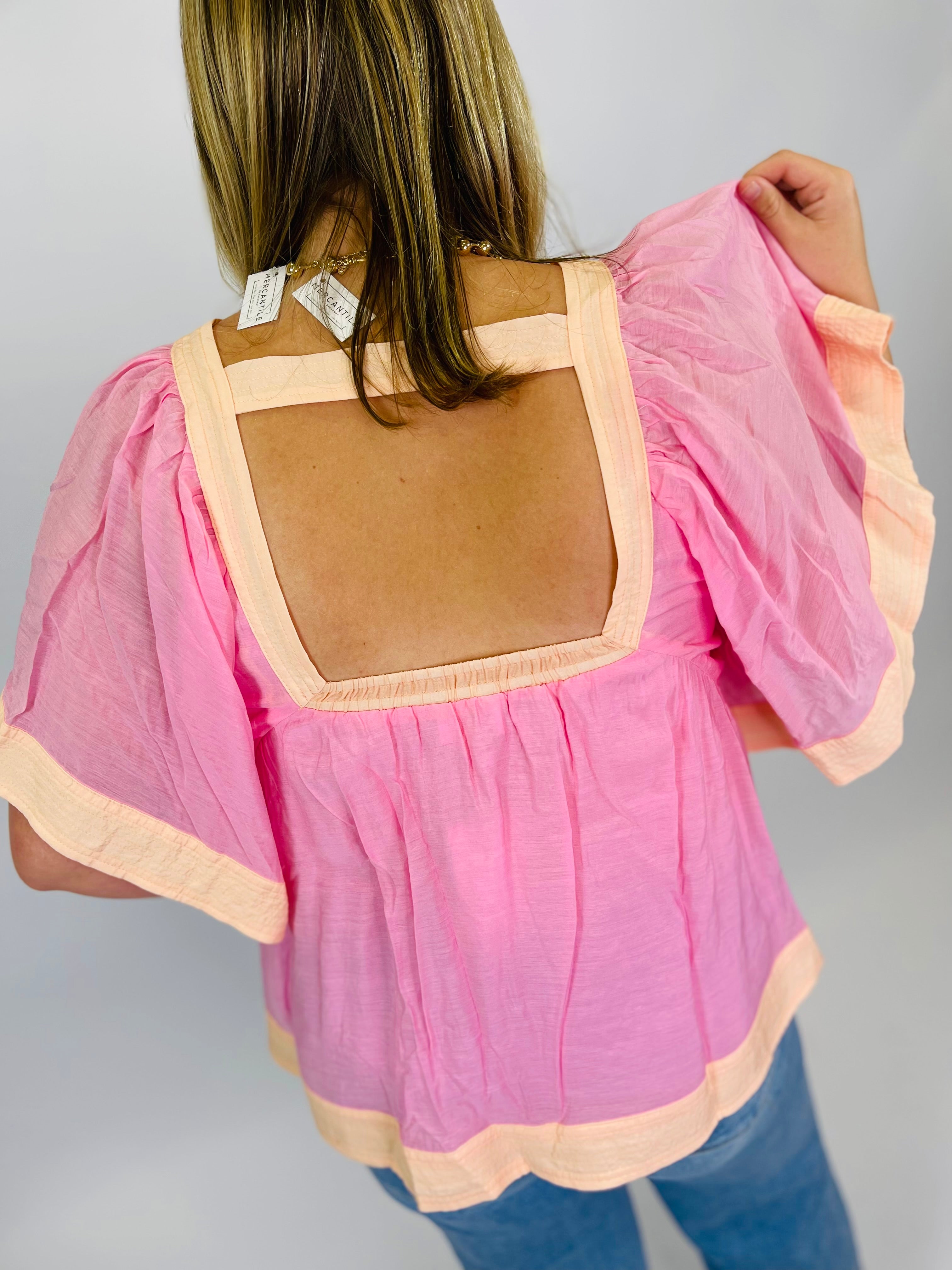 Pink off-shoulder top with peach trim and square neckline, back view showing open back detail.