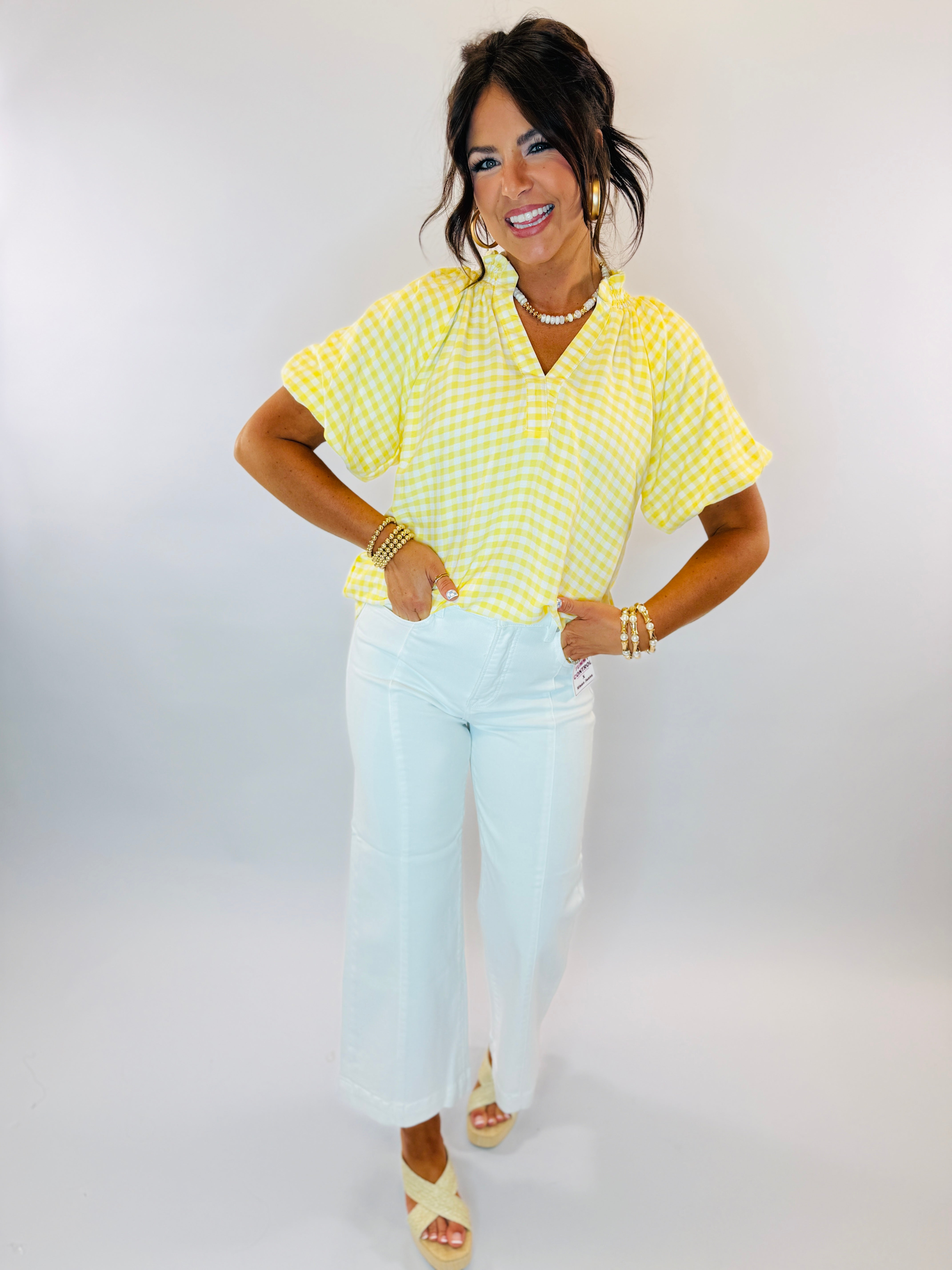 Woman wearing yellow and white gingham checkered short-sleeve top with white pants and pearl necklace