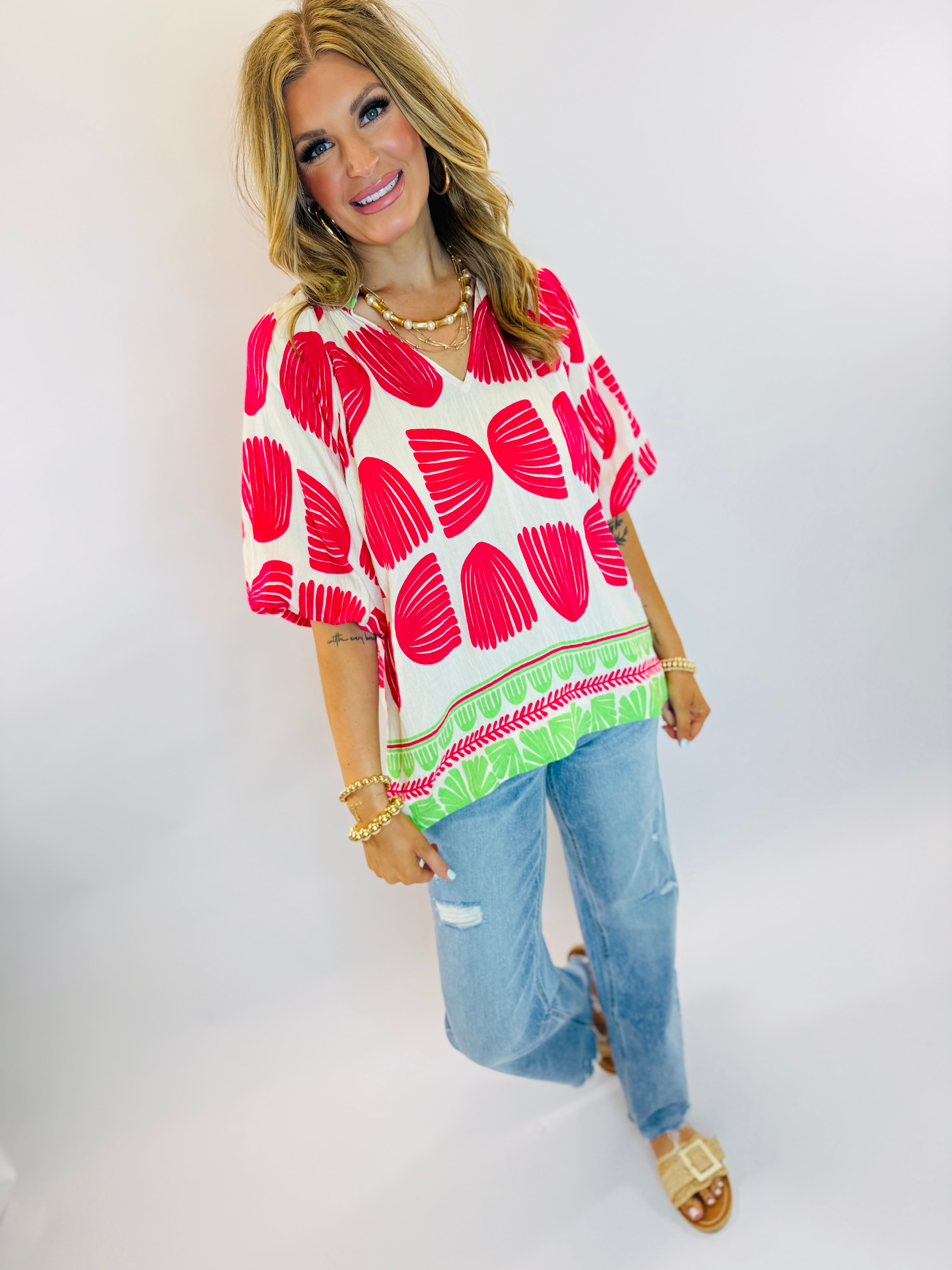 Woman wearing Rosa top with red polka dot pattern and green trim border paired with distressed jeans