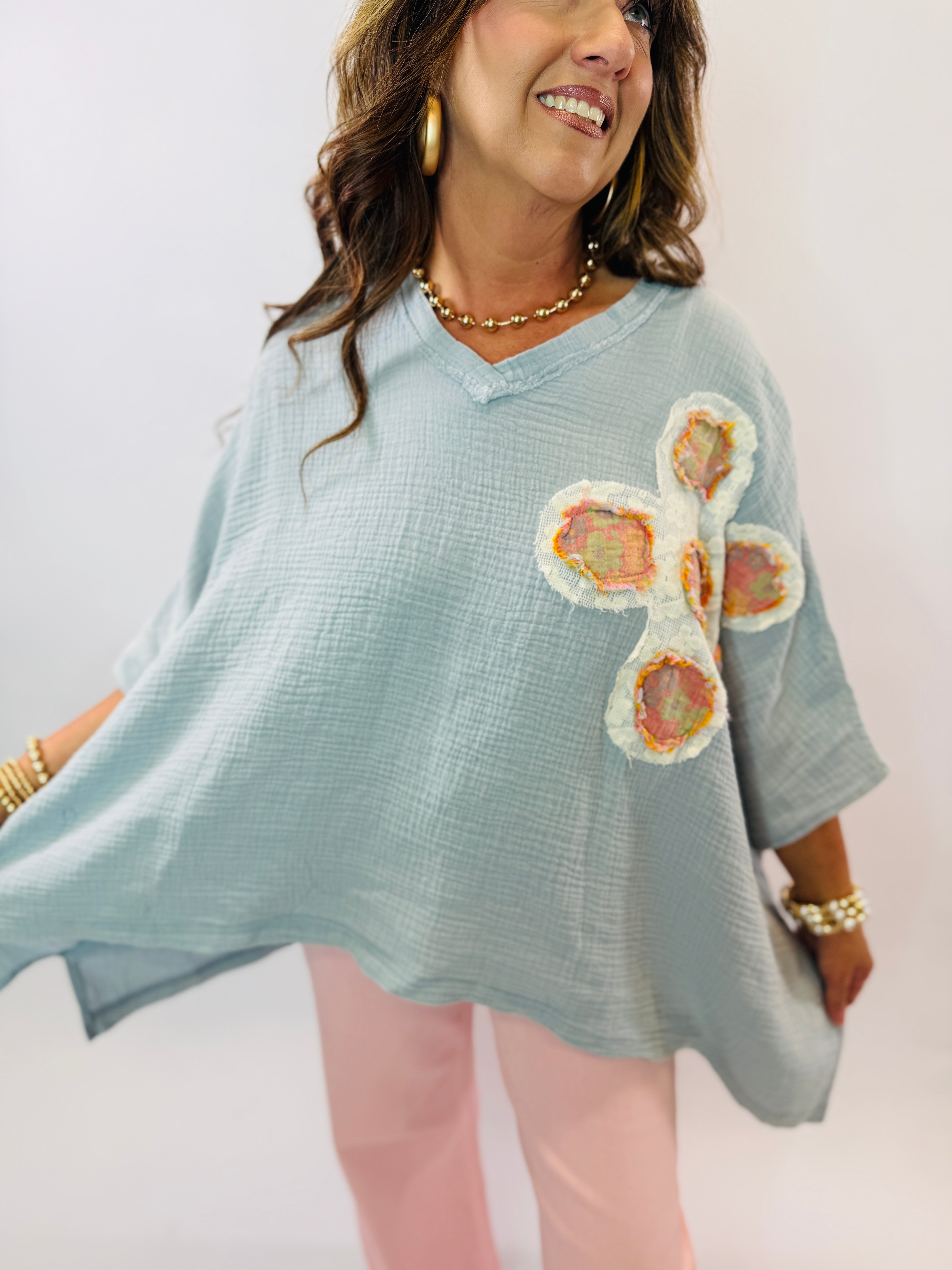 Woman wearing light blue gauze top with colorful floral appliqué patches and v-neck design