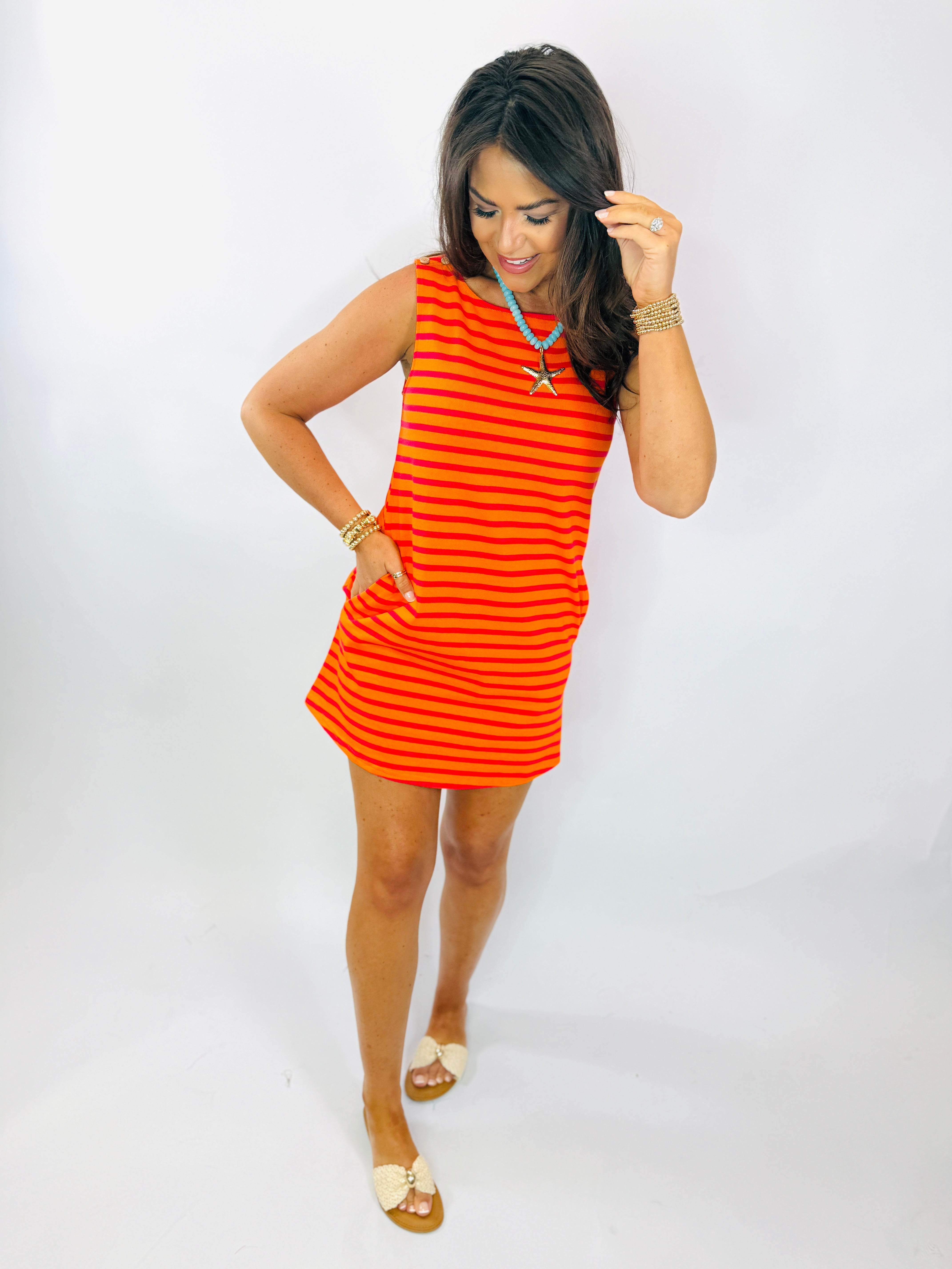 Woman wearing red and orange striped sleeveless Ali dress with turquoise necklace and gold accessories.