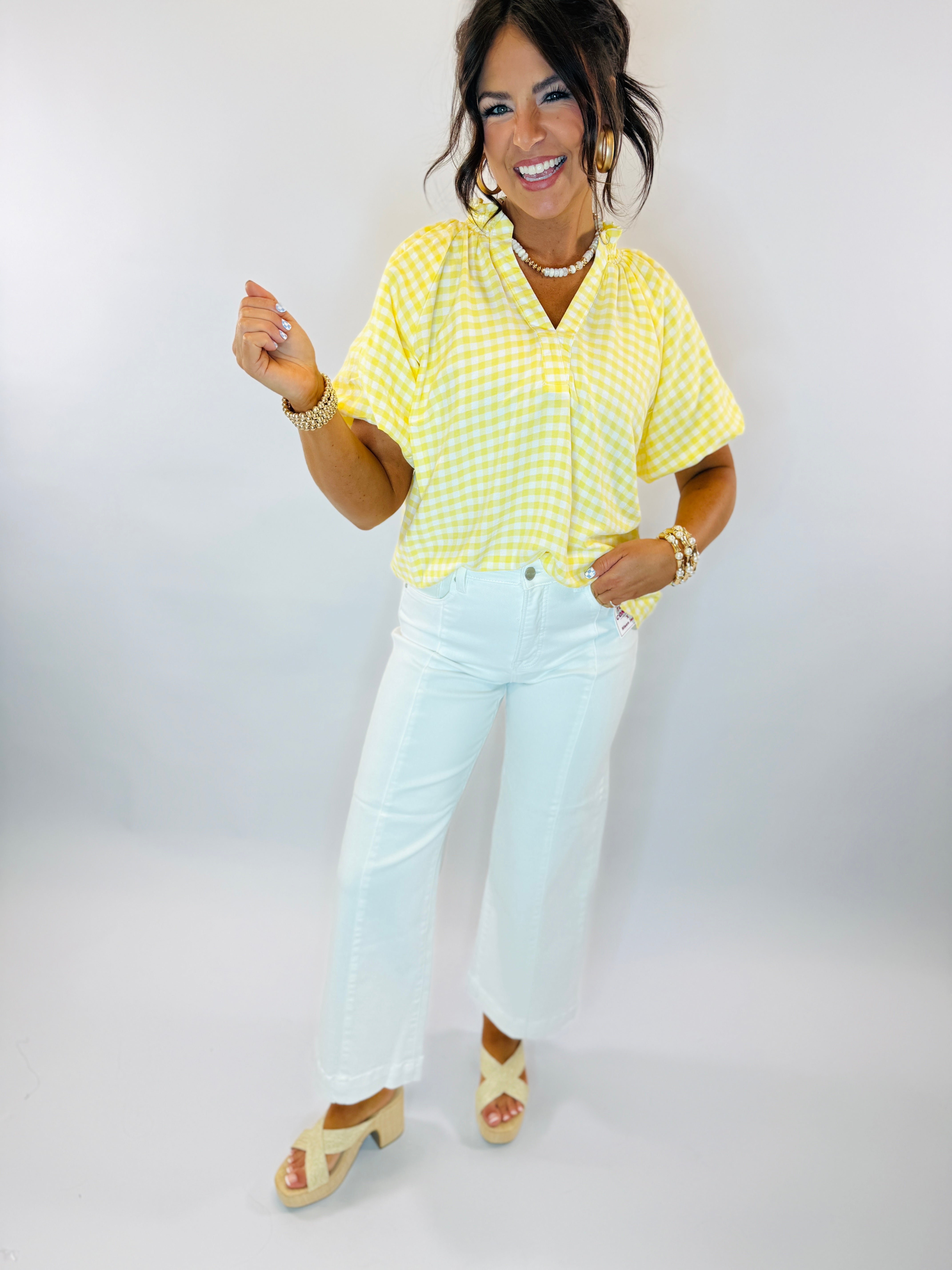 Woman wearing yellow and white gingham checkered short-sleeve button-up top with white jeans and sandals