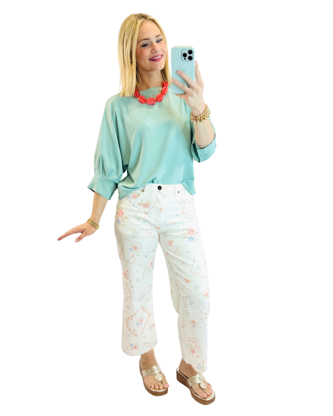 Woman wearing mint green Riley top with floral white jeans, taking mirror selfie with accessories