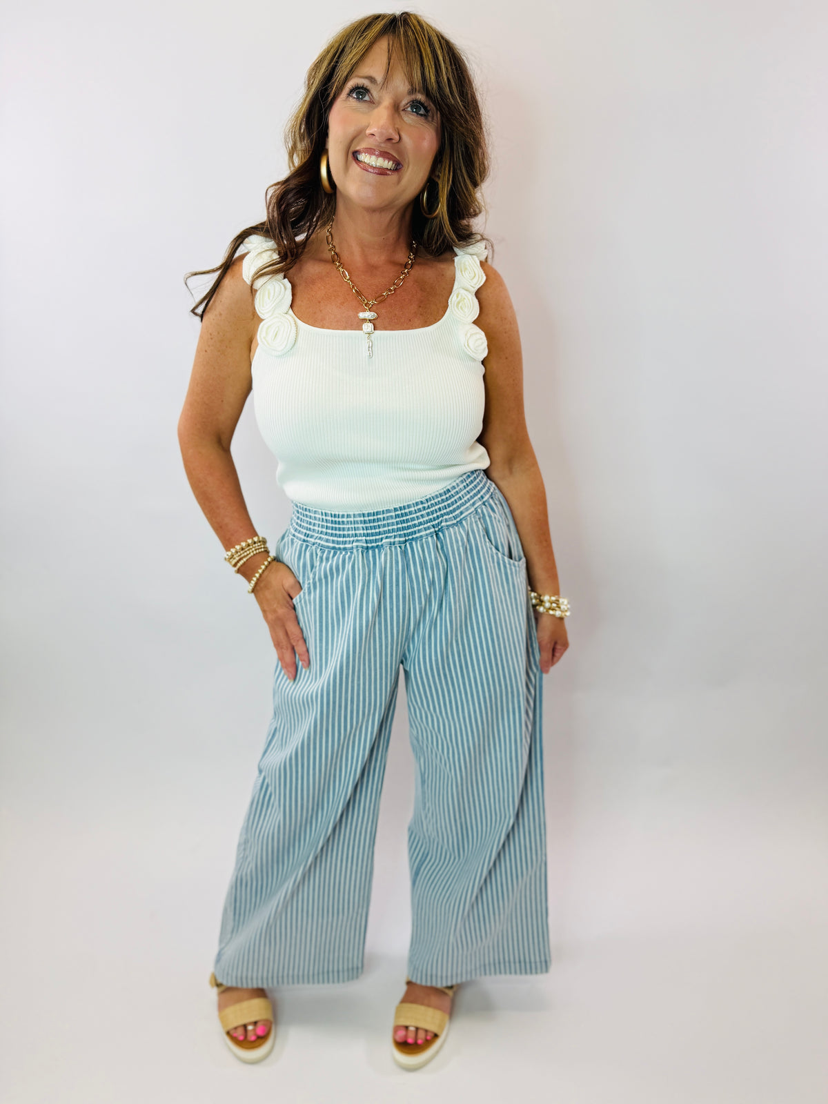 Woman wearing white ribbed tank top with ruffled straps, blue striped wide-leg pants, and gold jewelry