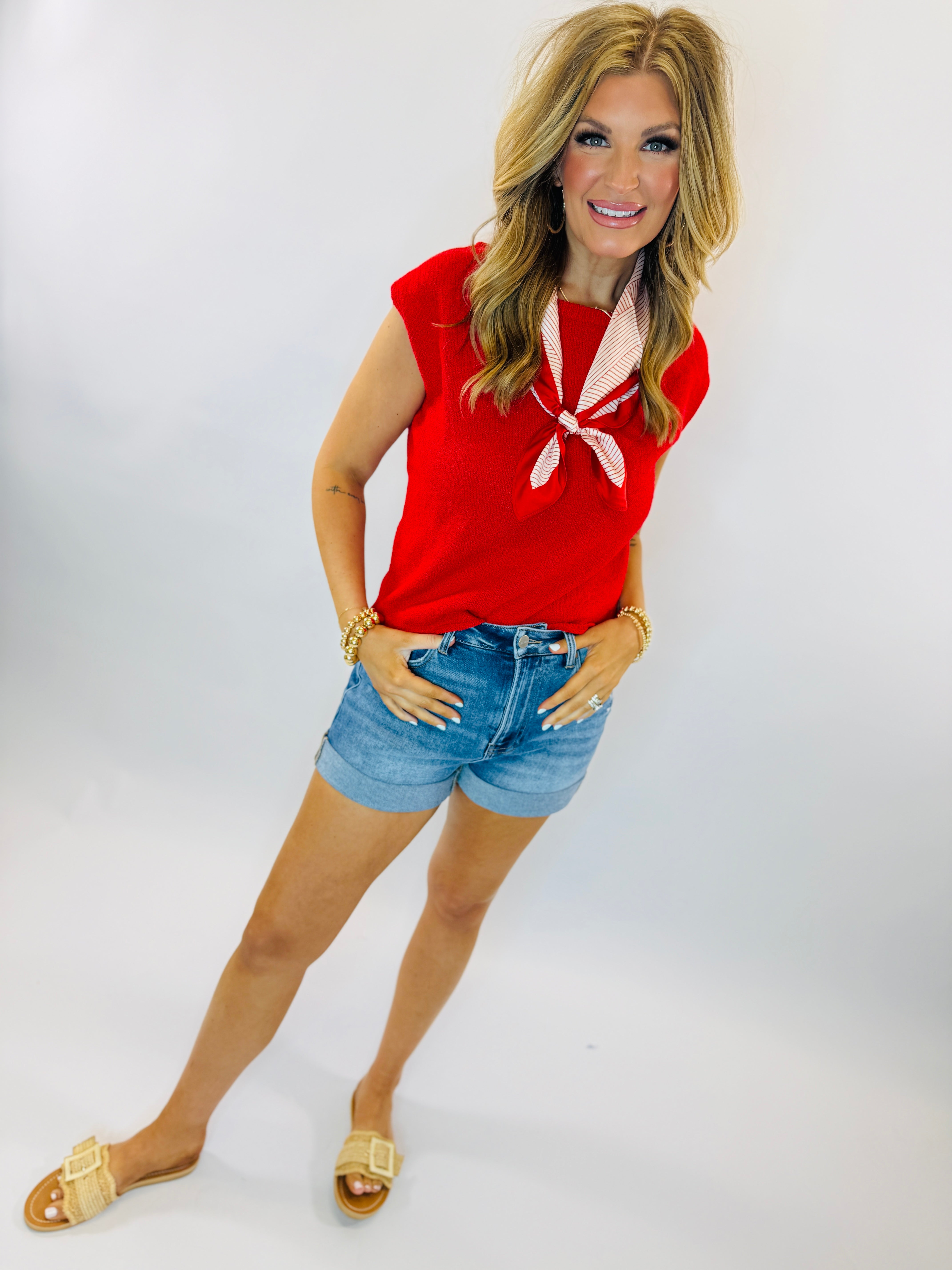 Woman wearing red sleeveless Pam sweater top with striped neck tie and denim shorts