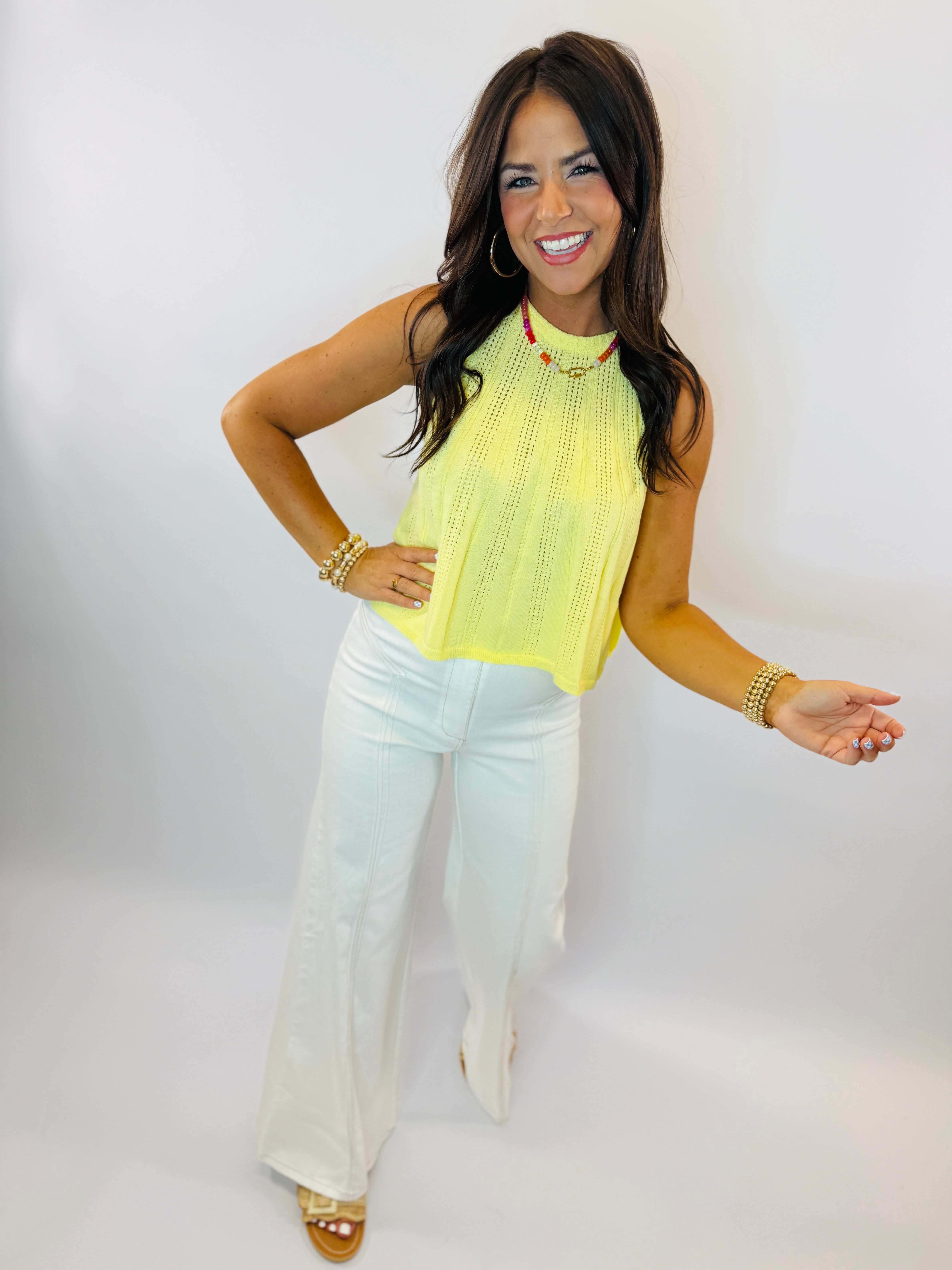 Woman wearing yellow sleeveless Grace top with crochet detailing and white flare jeans, posing with hand on hip.