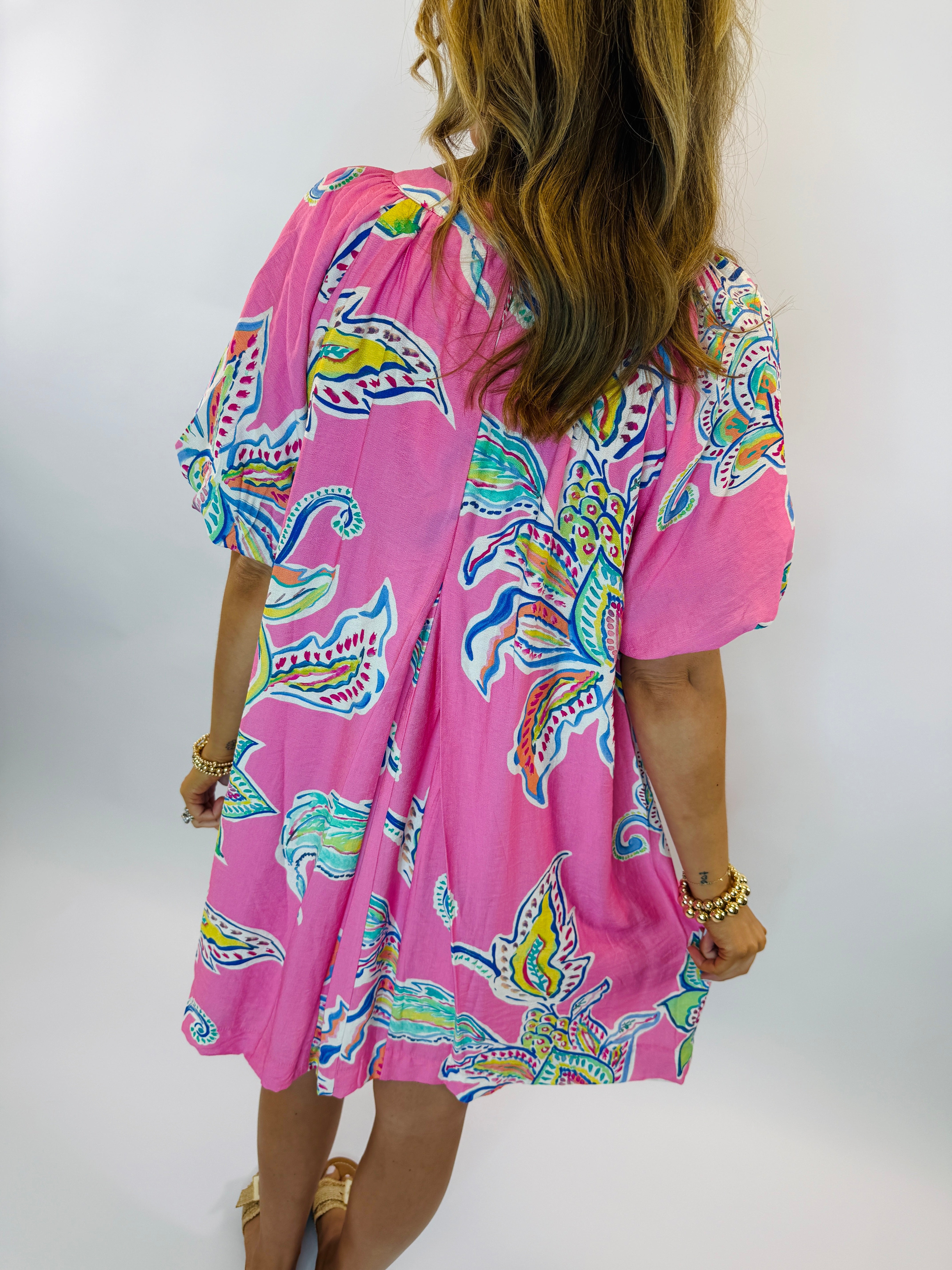Pink flowy dress with colorful paisley print, short sleeves, and knee-length hemline worn by model