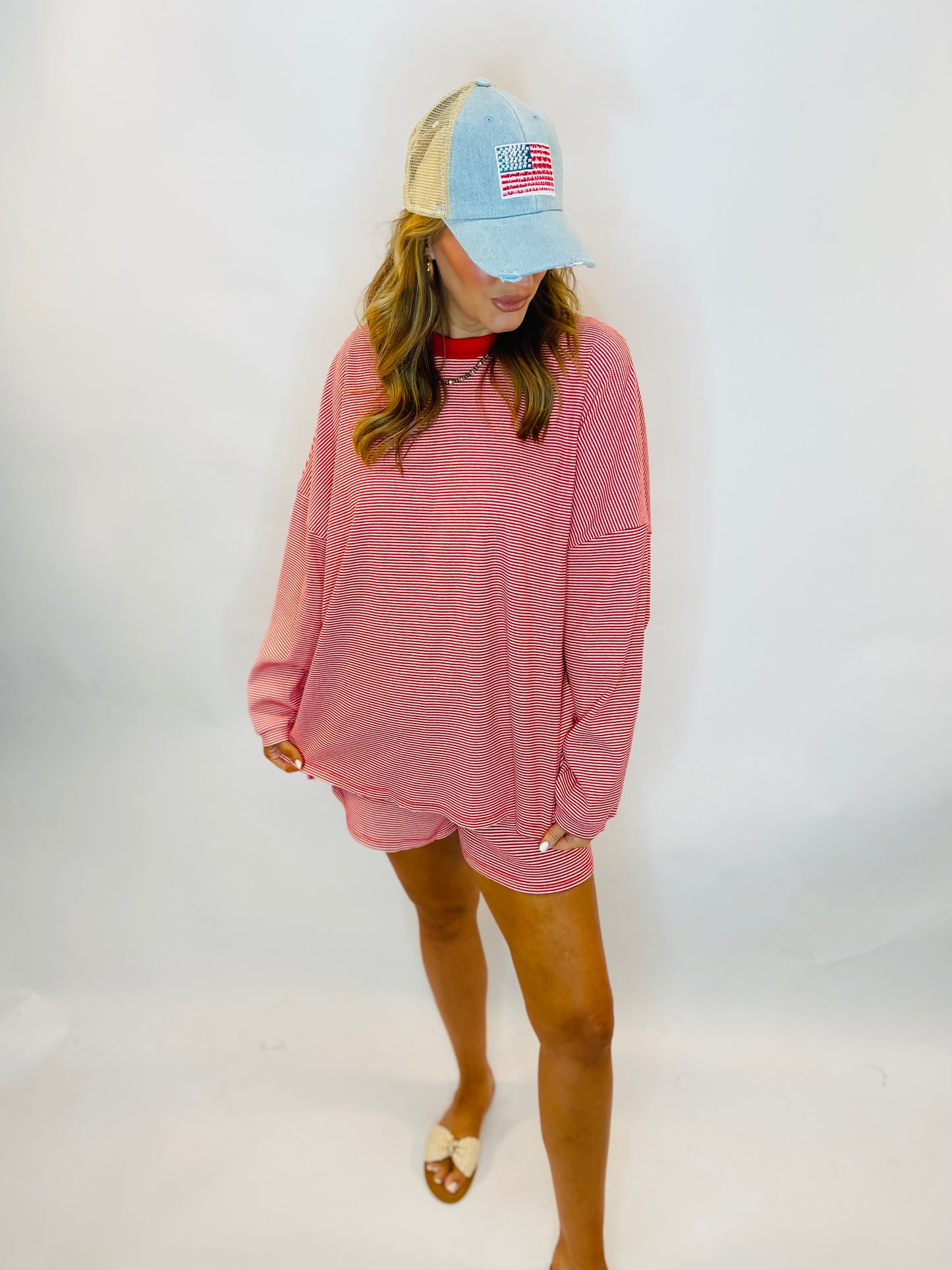 Oversized red and white striped long-sleeve top paired with matching shorts and an American flag baseball cap.