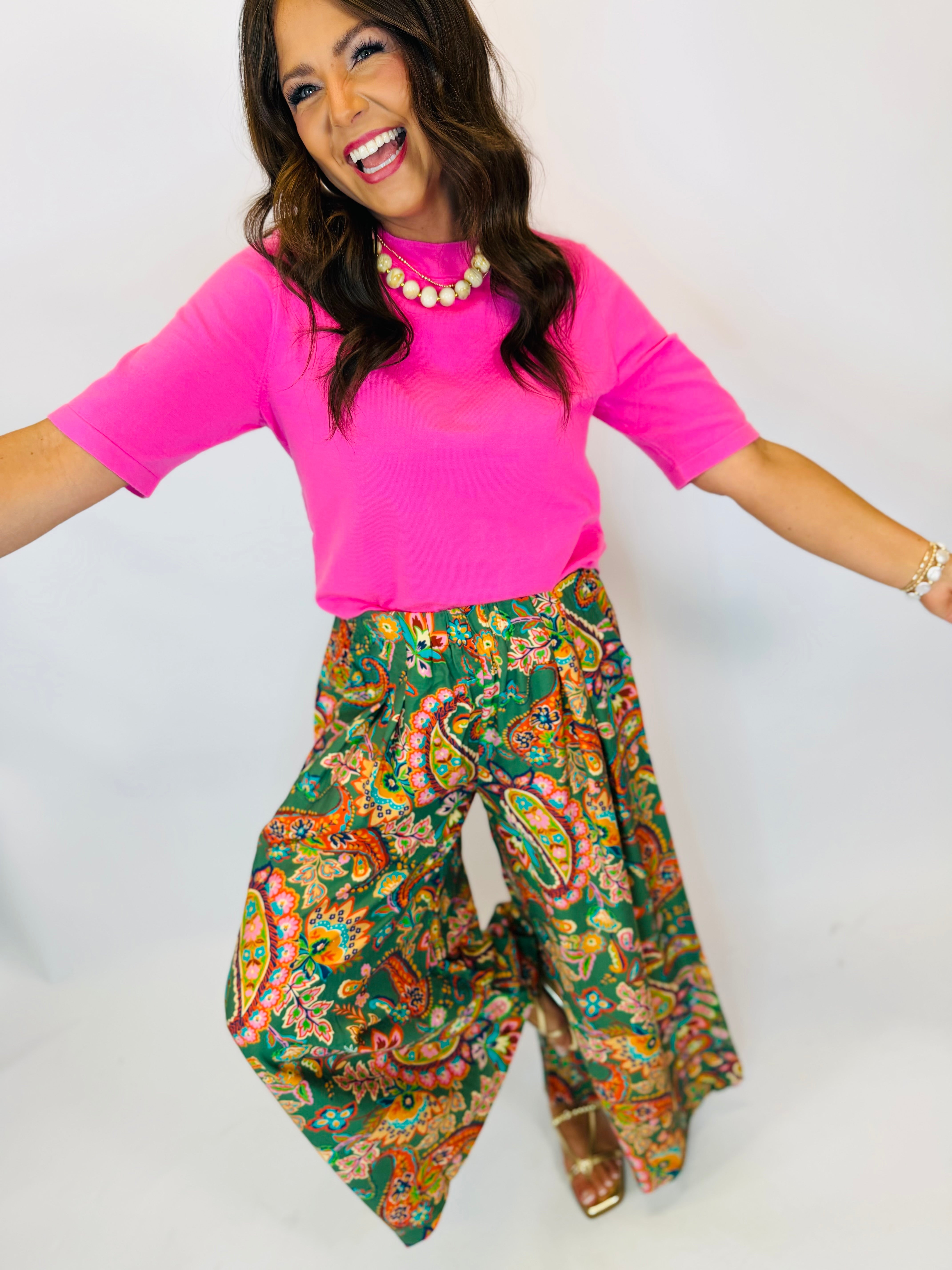 Woman wearing bright pink short-sleeve mock-neck sweater top paired with colorful paisley wide-leg pants.