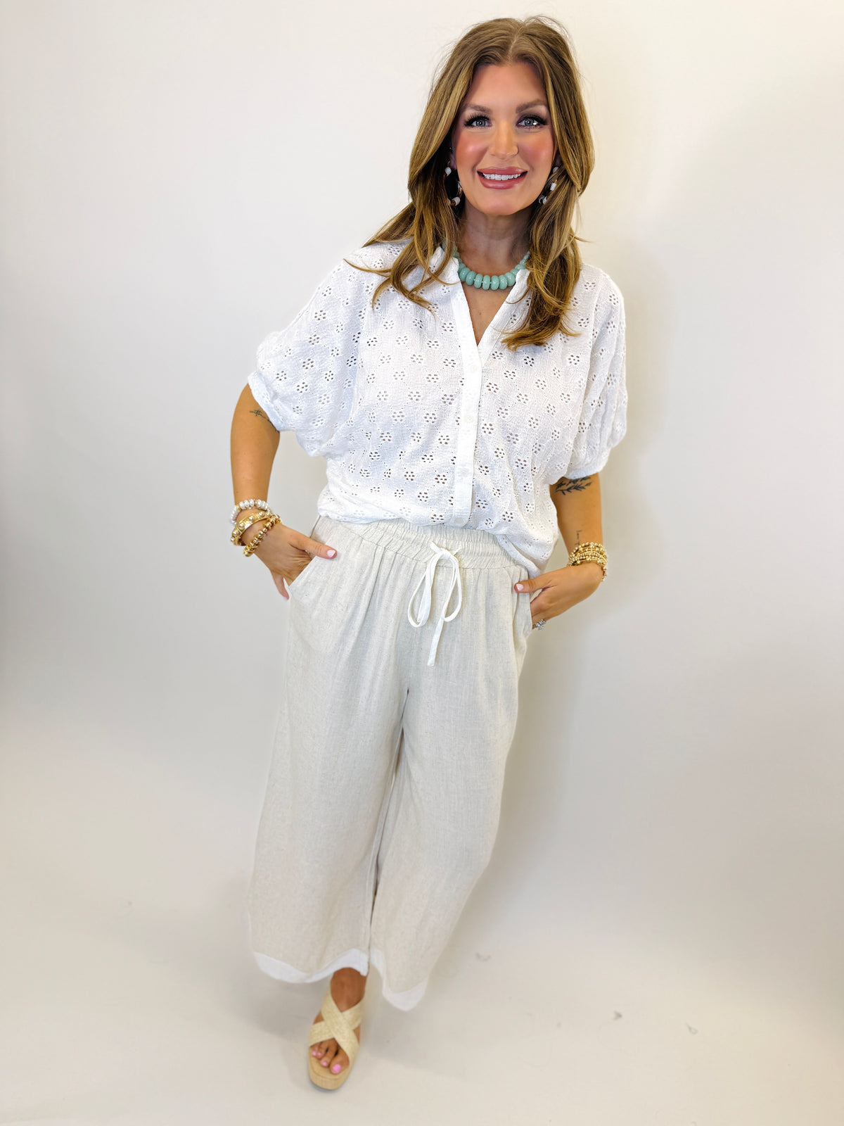 Woman wearing white eyelet lace short-sleeve button-up top with relaxed fit and decorative perforated pattern.