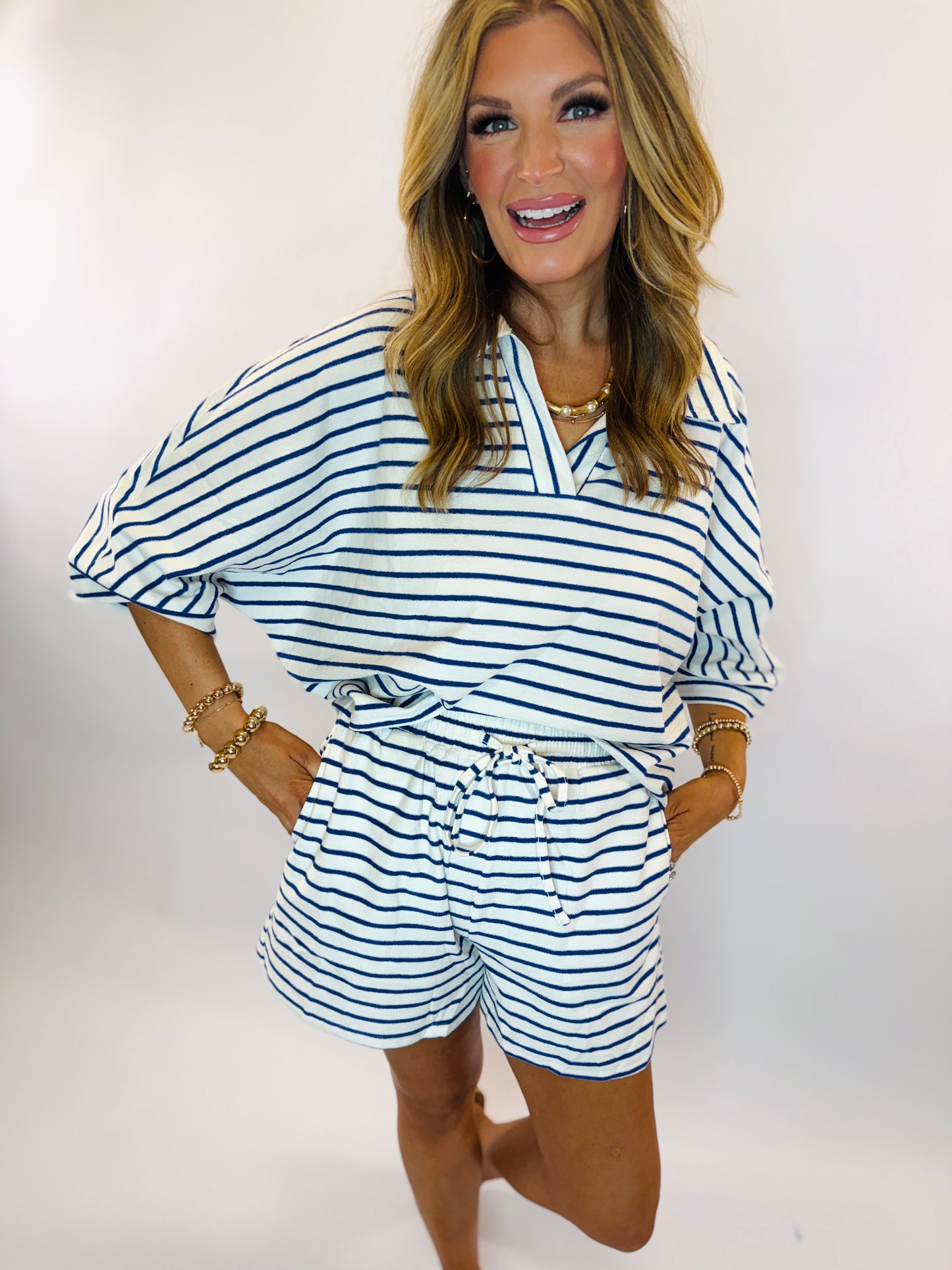 Woman wearing blue and white striped matching set with relaxed top and drawstring shorts, accessorized with gold jewelry.