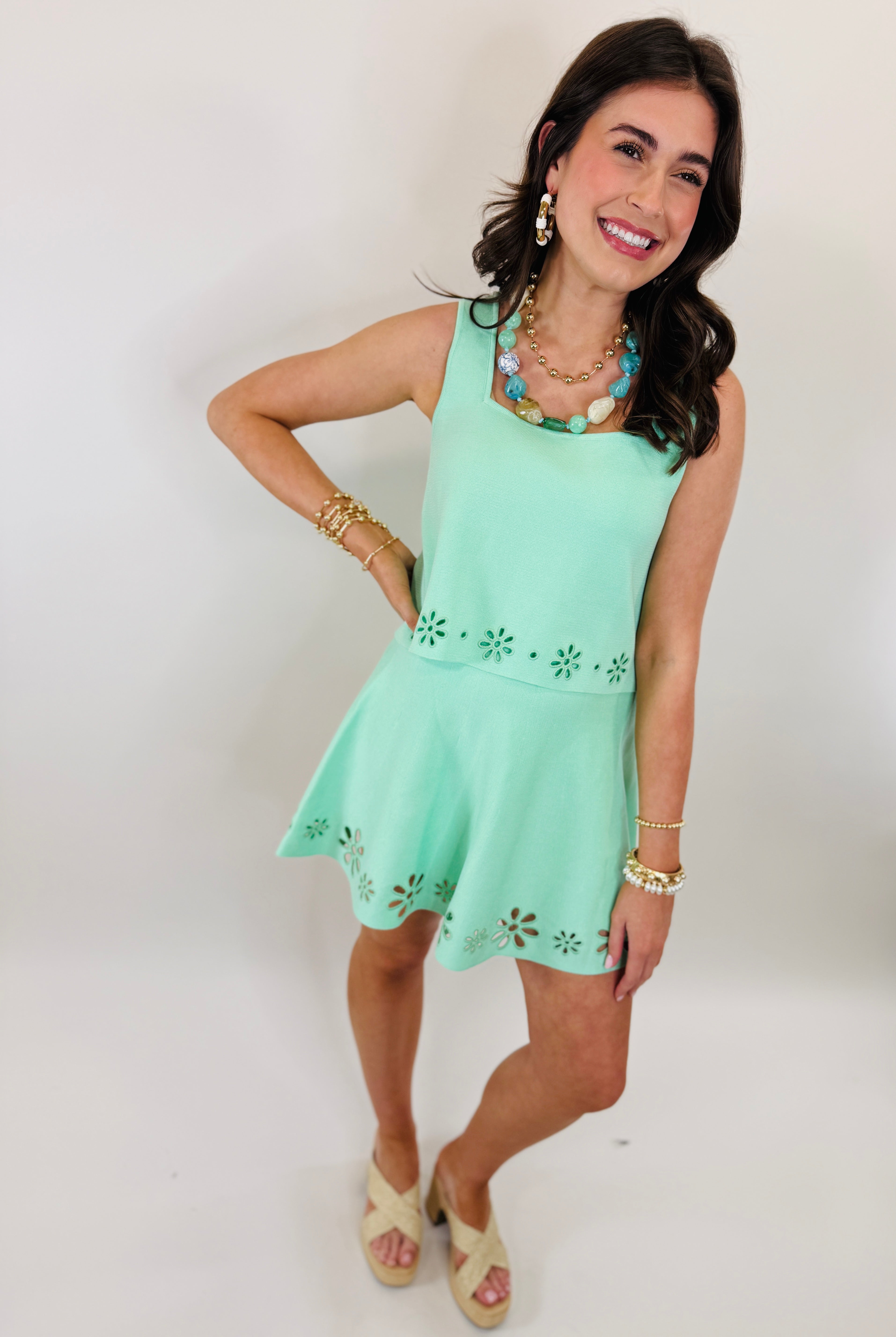 Woman wearing mint green sleeveless top and matching skirt set with laser-cut floral details, styled with layered jewelry.