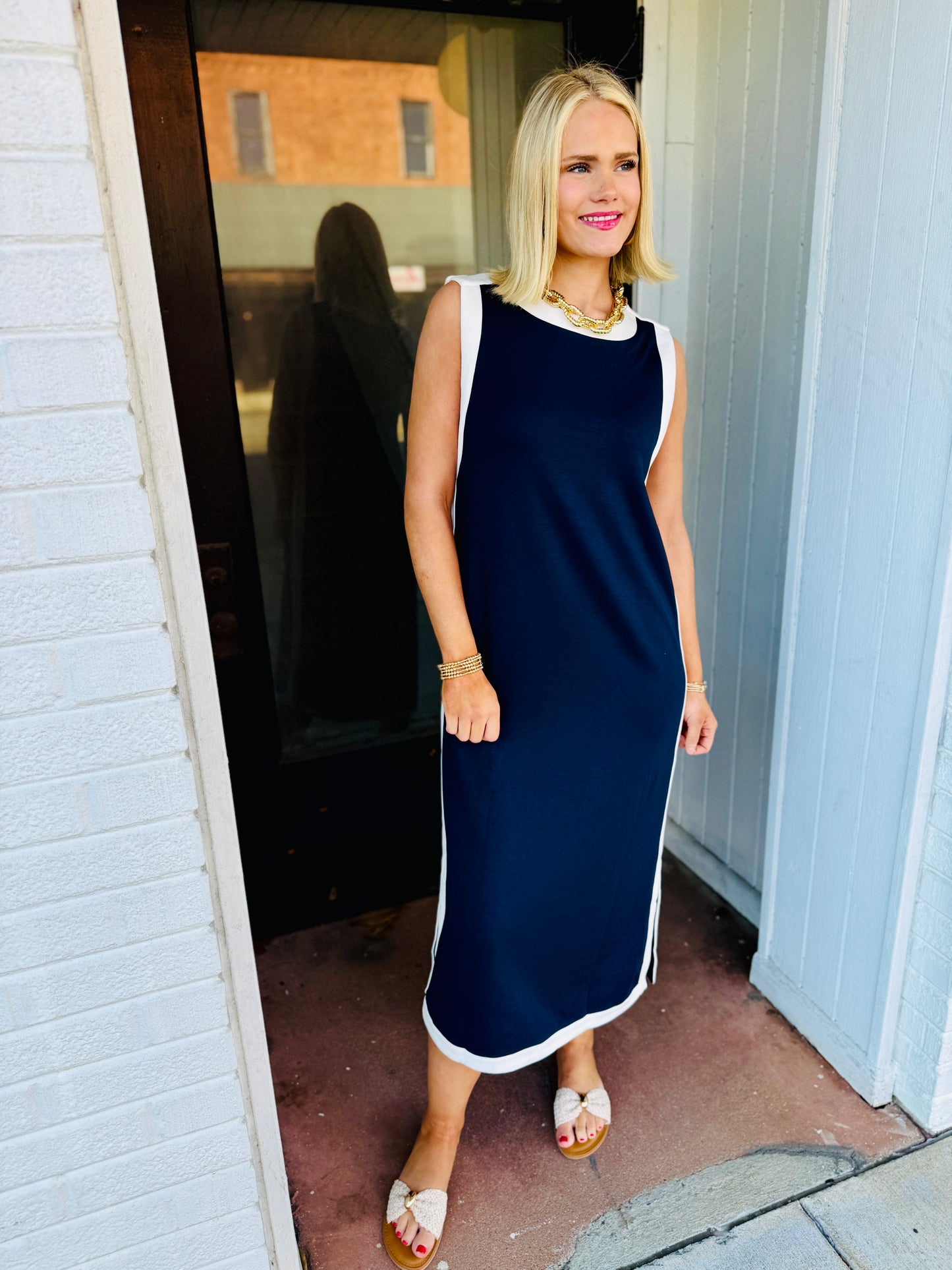 Woman wearing navy blue sleeveless midi dress with white trim and gold jewelry accessories