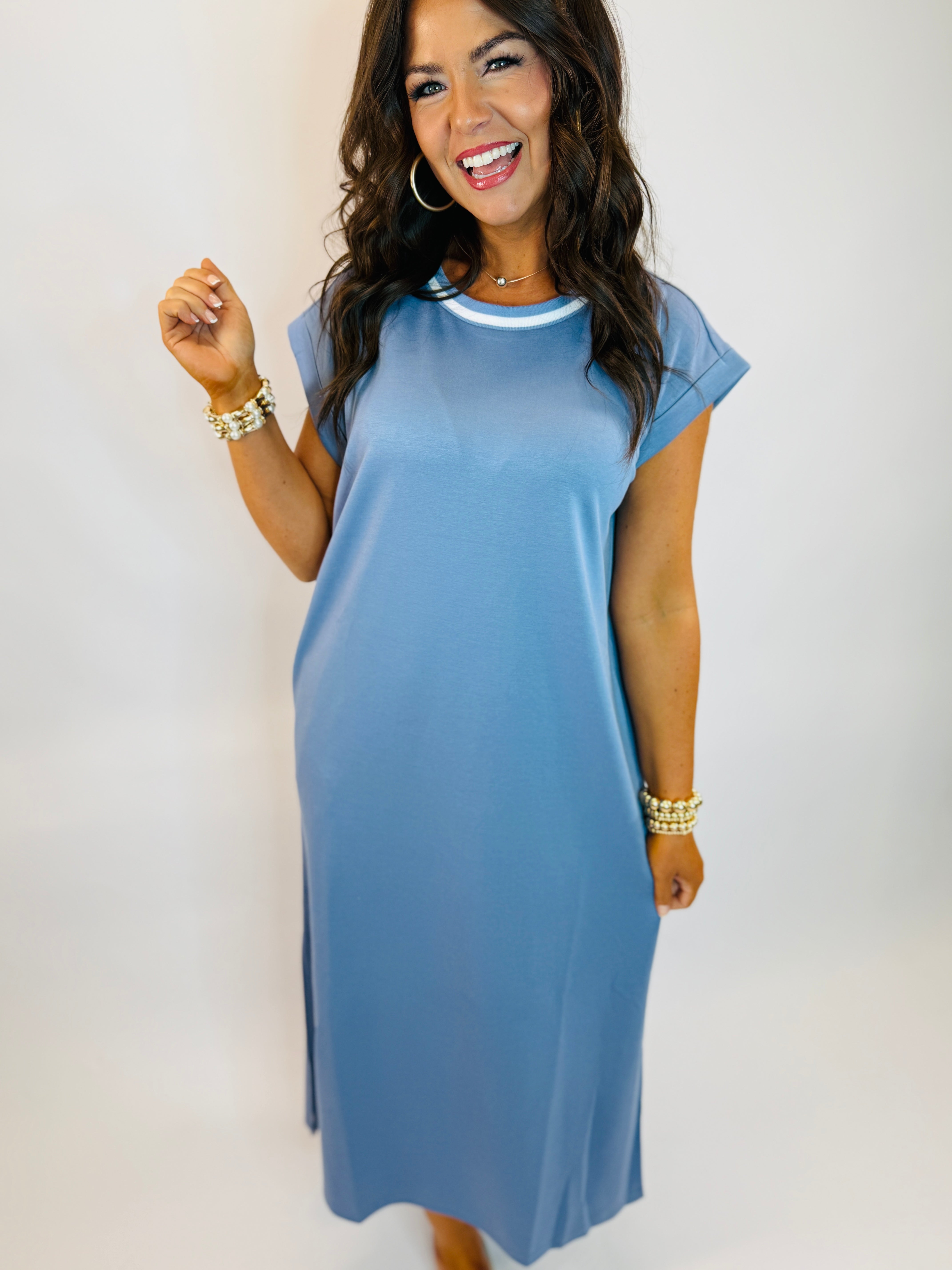 Woman wearing blue midi t-shirt dress with white trim neckline, pearl bracelets, and hoop earrings