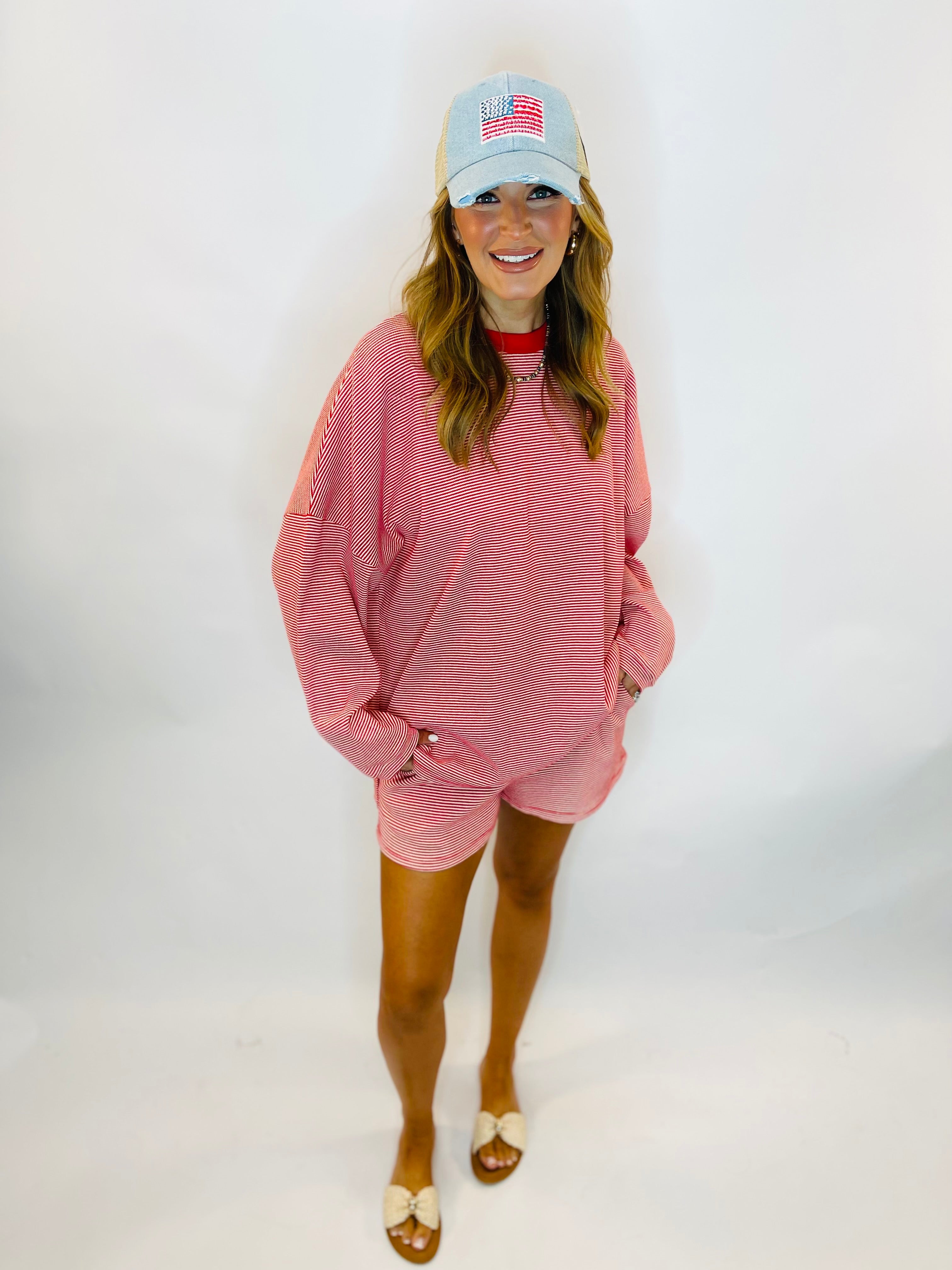 Red and white striped oversized long sleeve top worn with matching shorts and American flag cap.
