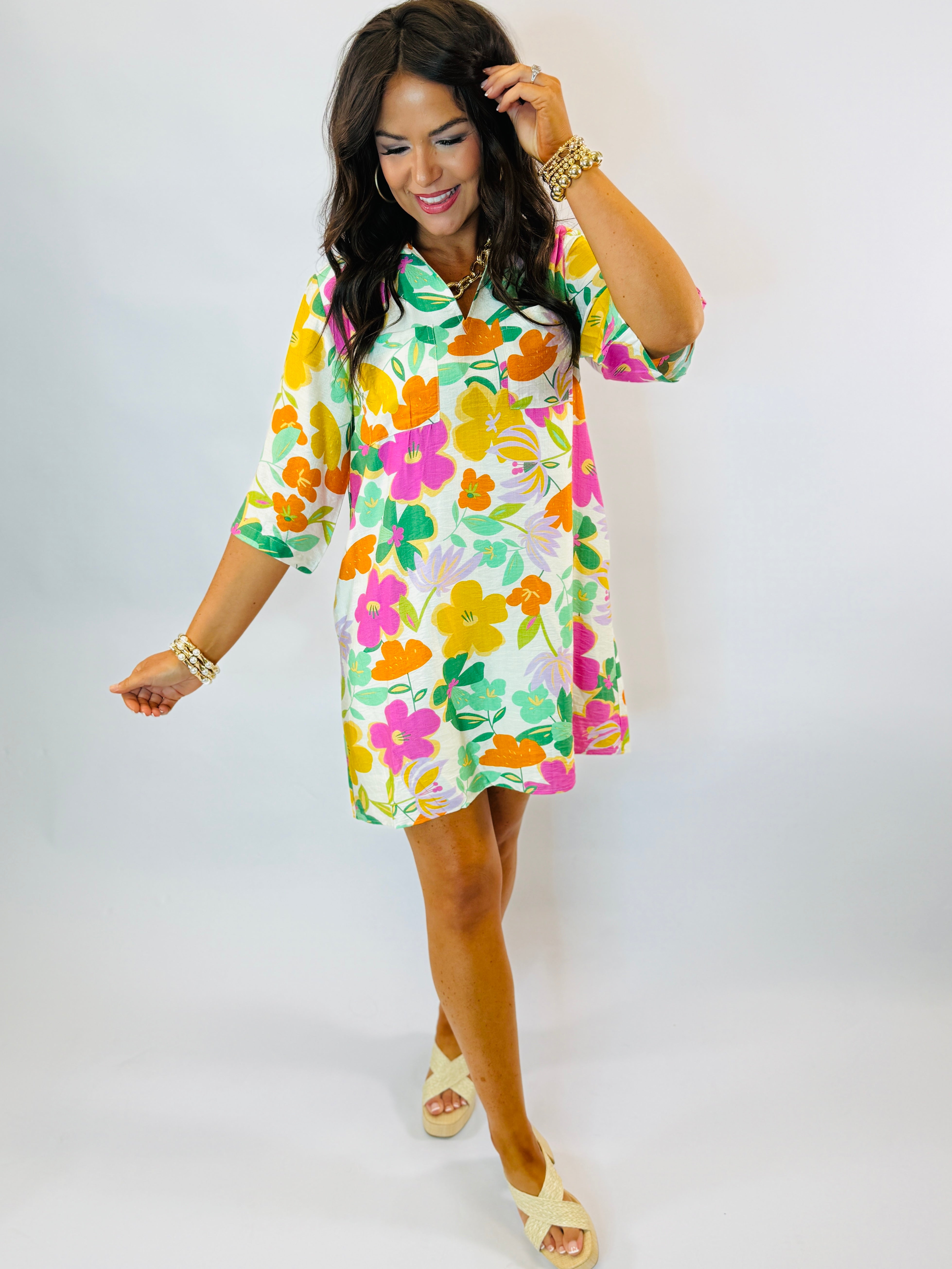 Woman wearing colorful floral print Gloria dress with three-quarter sleeves, paired with gold jewelry and cream platform s...