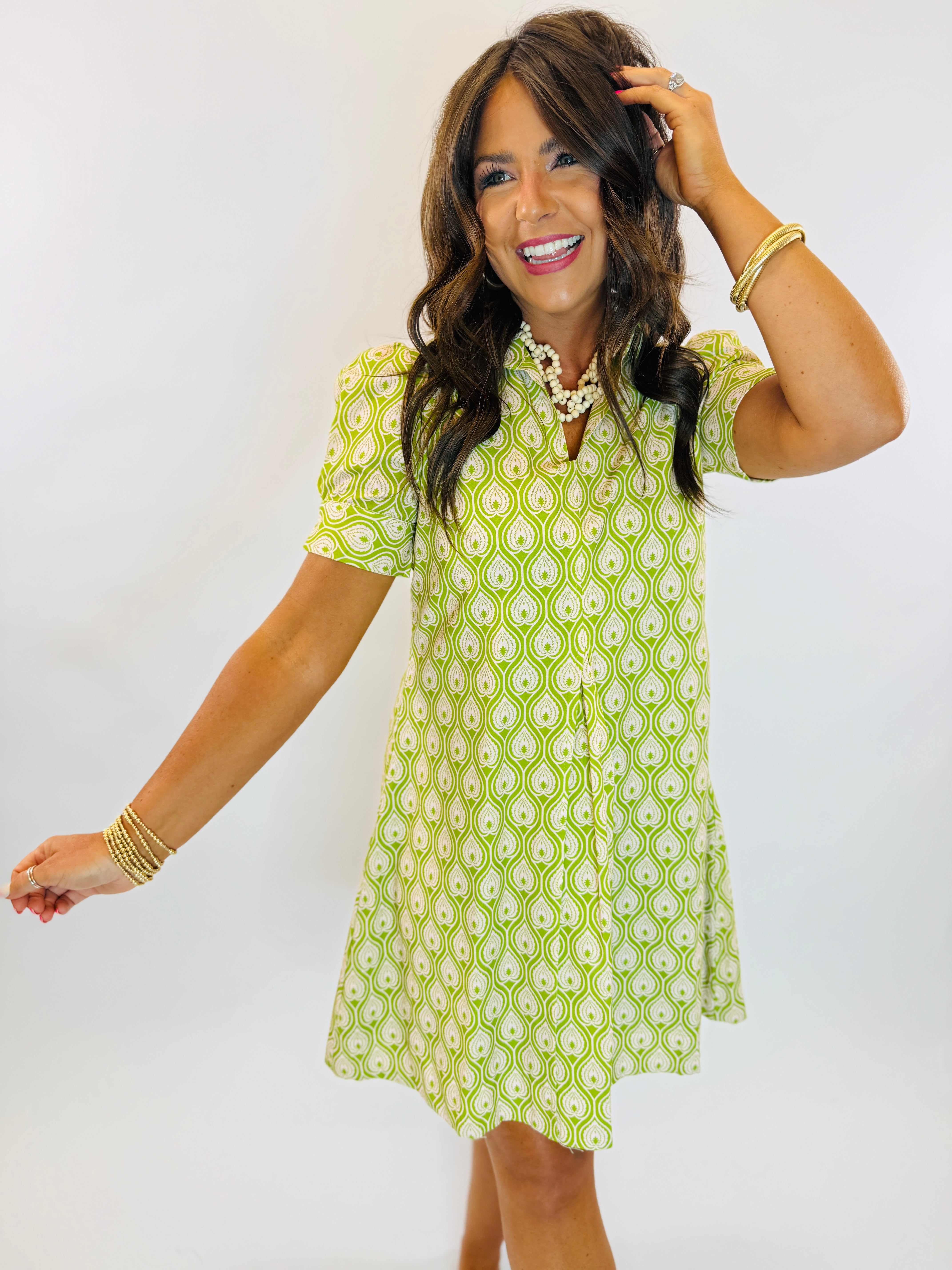Woman wearing the Lisa Dress, a green and white paisley print short-sleeve mini dress with V-neckline.
