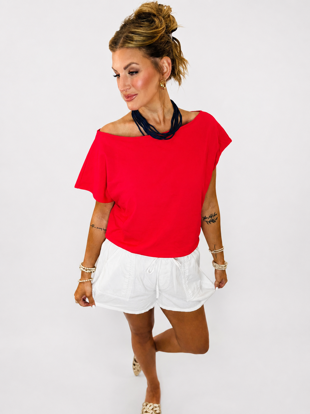 Woman wearing red off-shoulder short-sleeve Sami Top paired with white drawstring shorts.