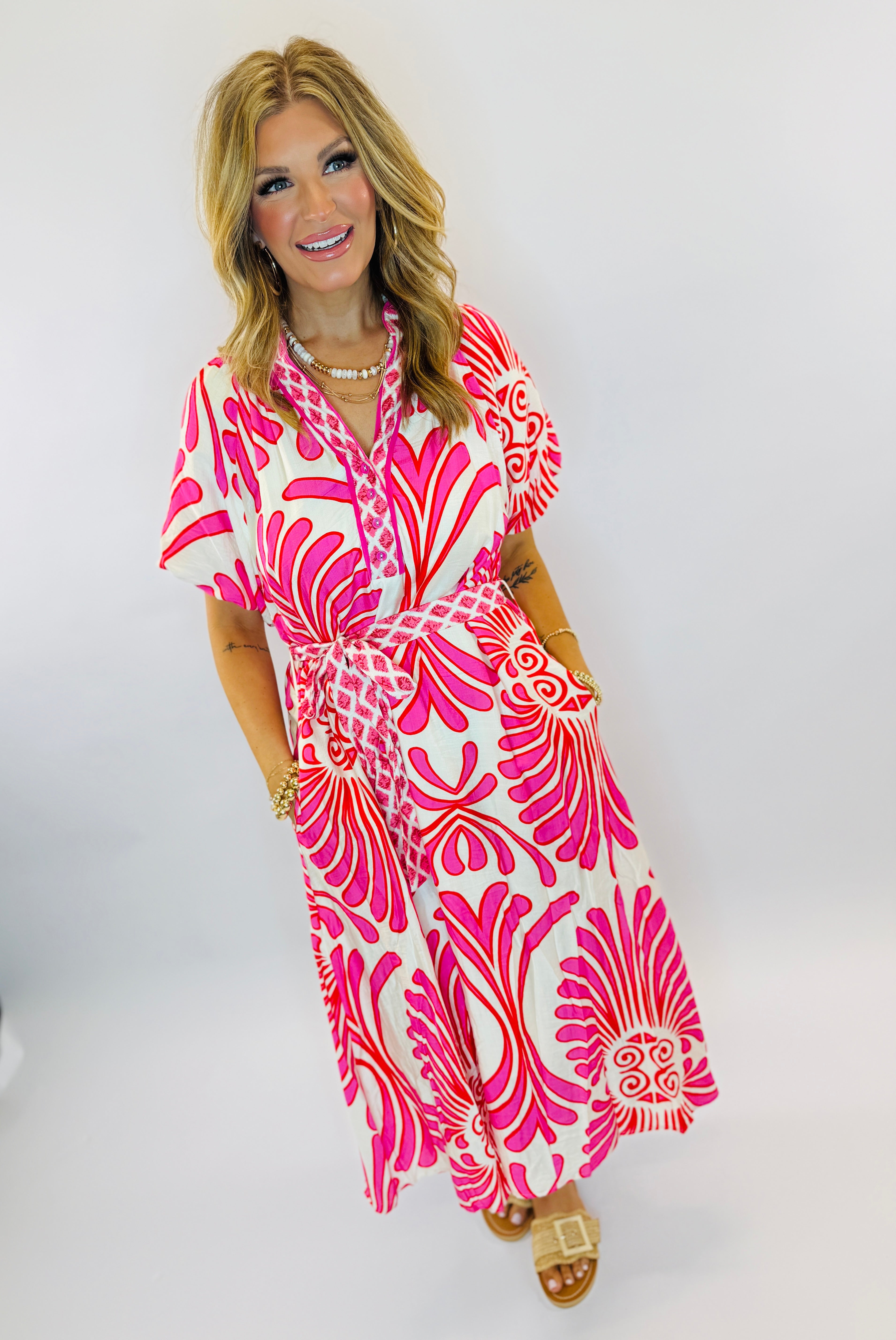 Woman wearing pink and white patterned Carmen dress with tropical print, belt tie, and short sleeves