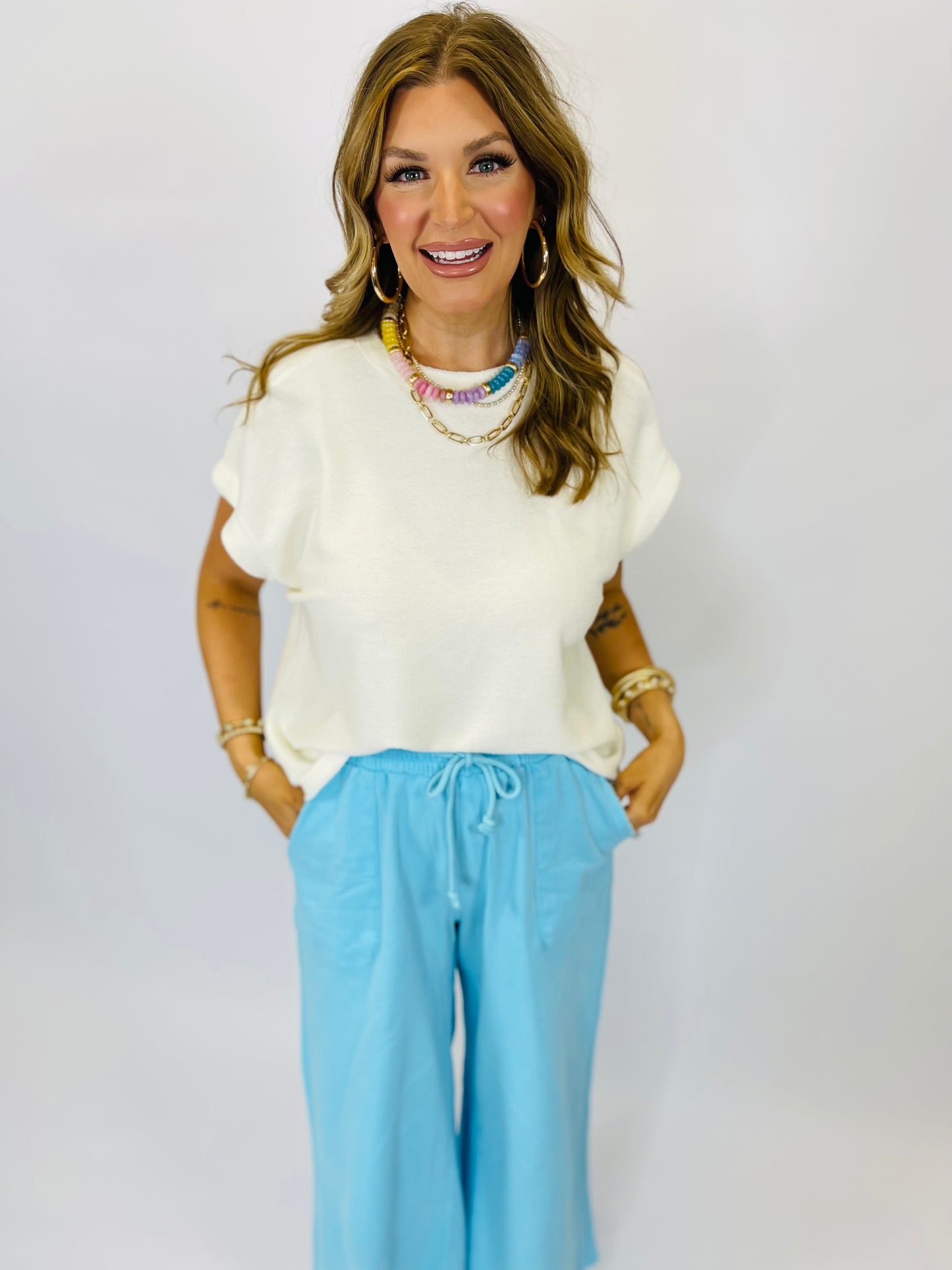 Woman wearing white short-sleeve Maya Classic Everyday Top with blue pants and colorful beaded necklace, smiling at camera