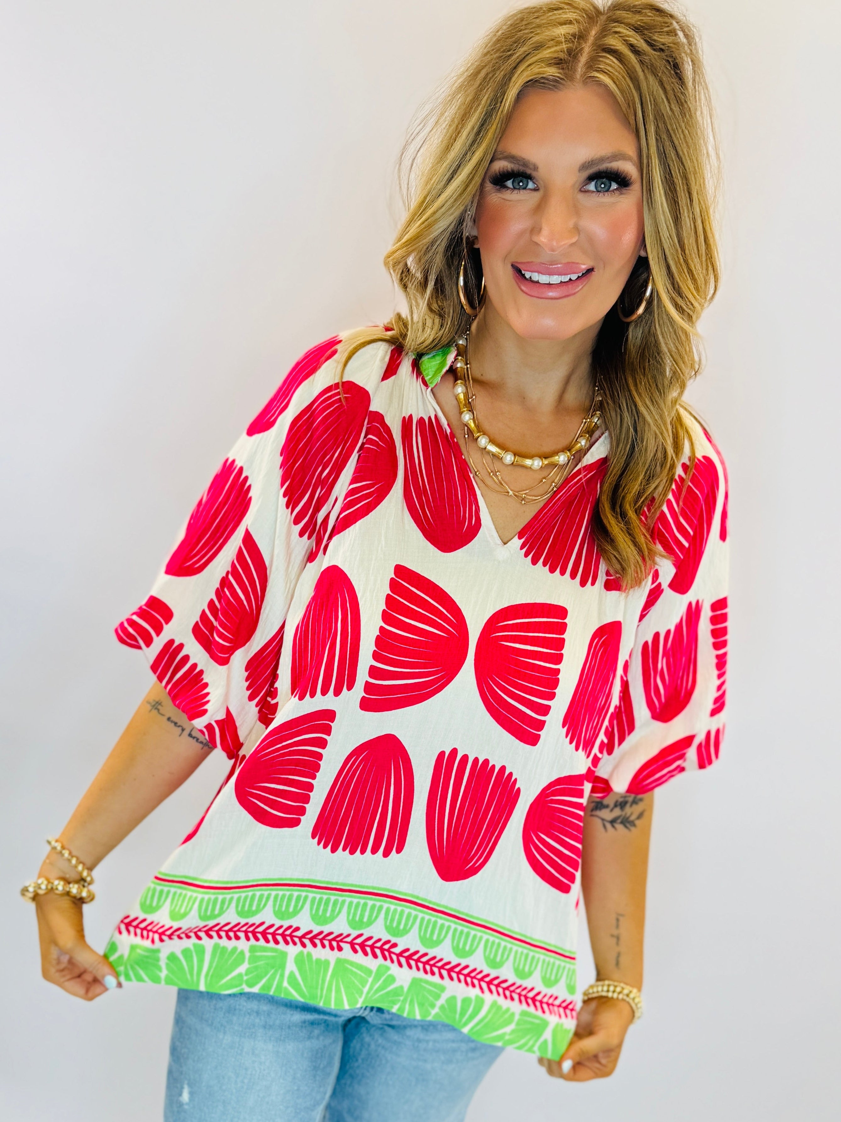 Woman wearing white Rosa top with large red floral print and green border detail, paired with jeans.