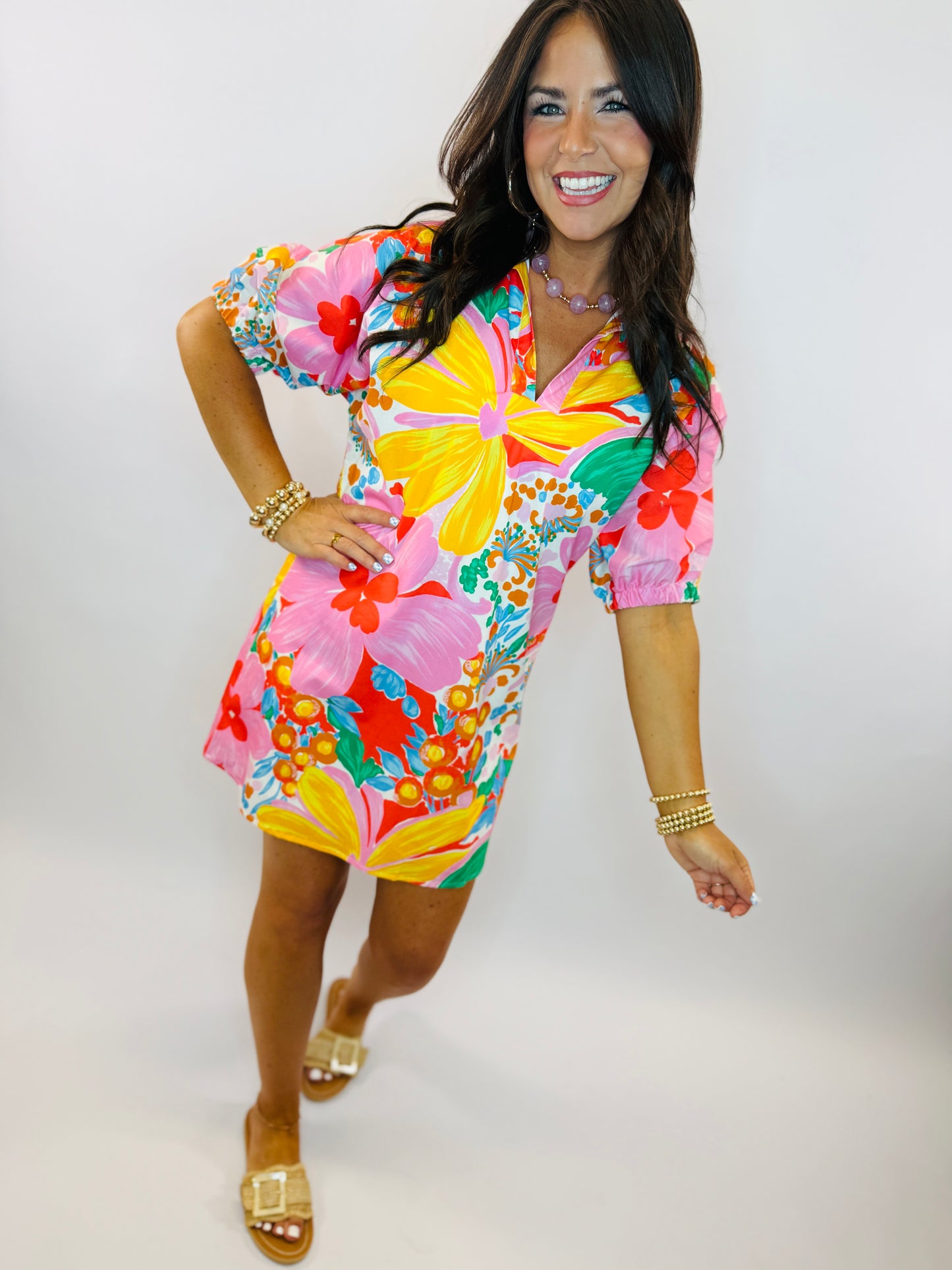 Woman wearing vibrant tropical floral print dress with short sleeves, featuring pink, yellow, and red hibiscus flowers.