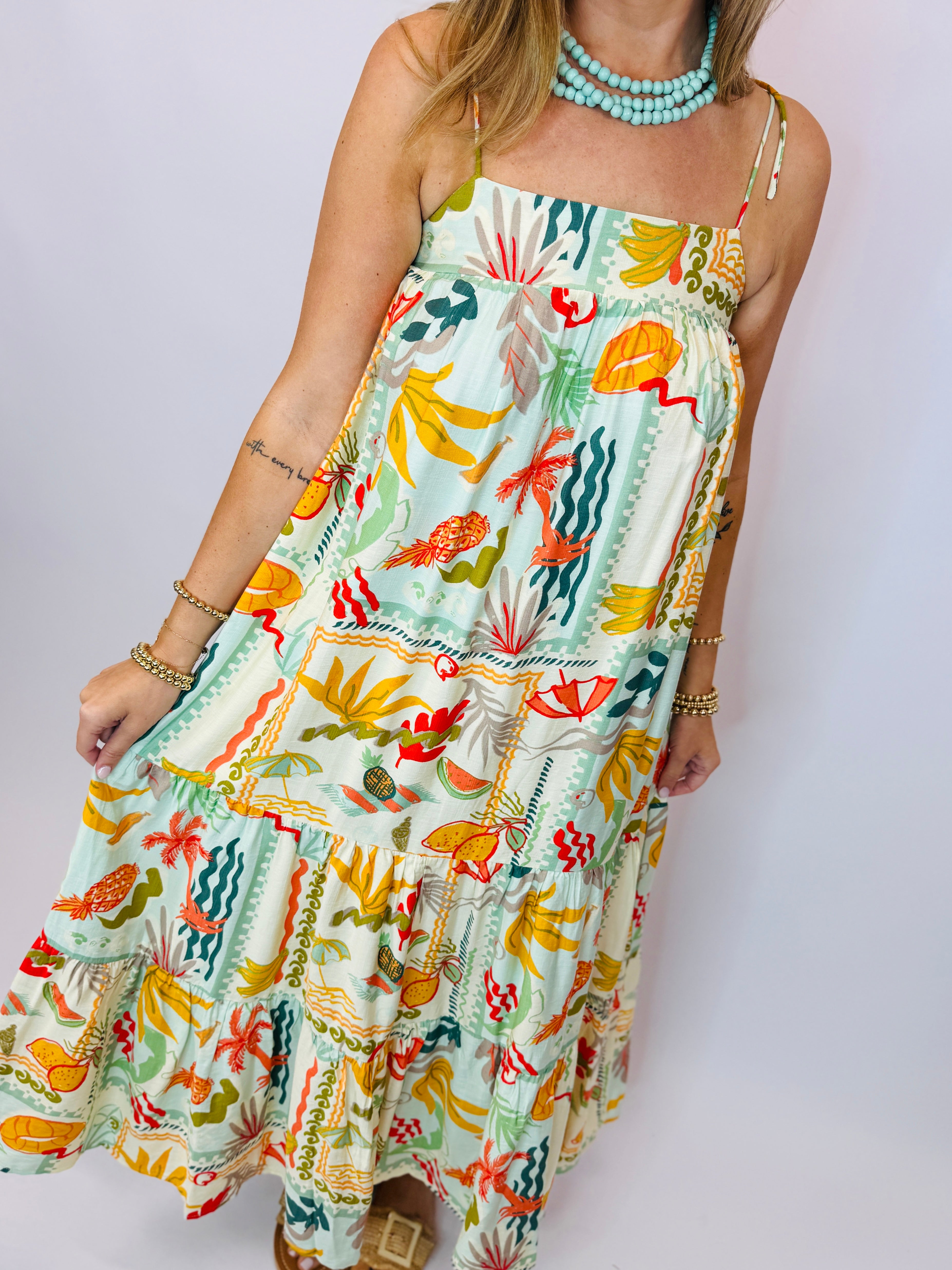 Colorful tropical print maxi dress with spaghetti straps and tiered ruffles, styled with turquoise beaded necklace