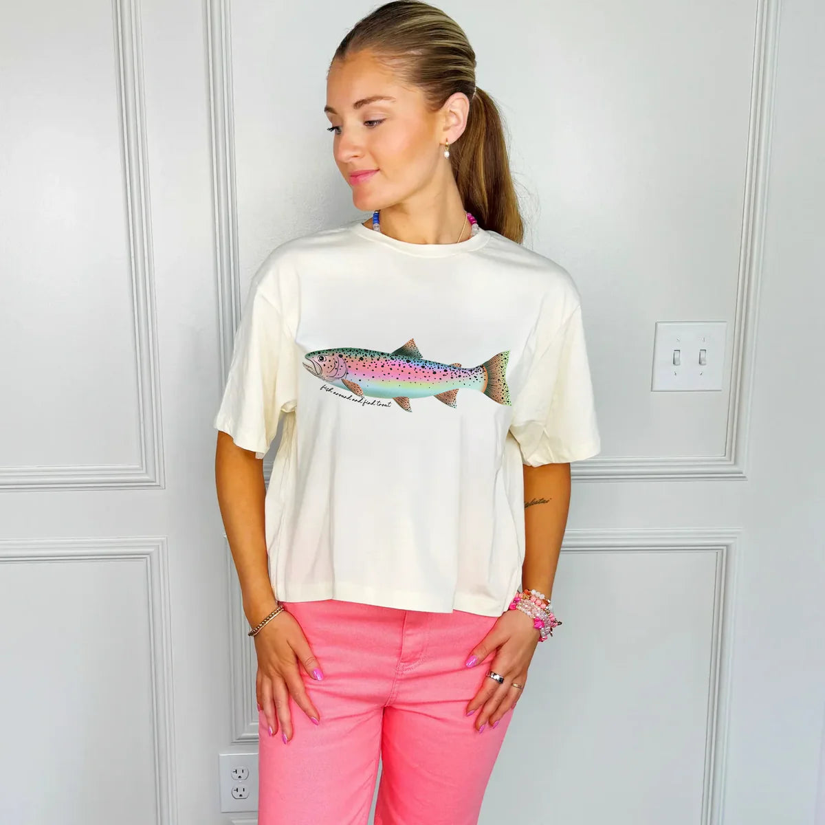 Woman wearing white cropped t-shirt with colorful rainbow trout graphic and bright pink pants
